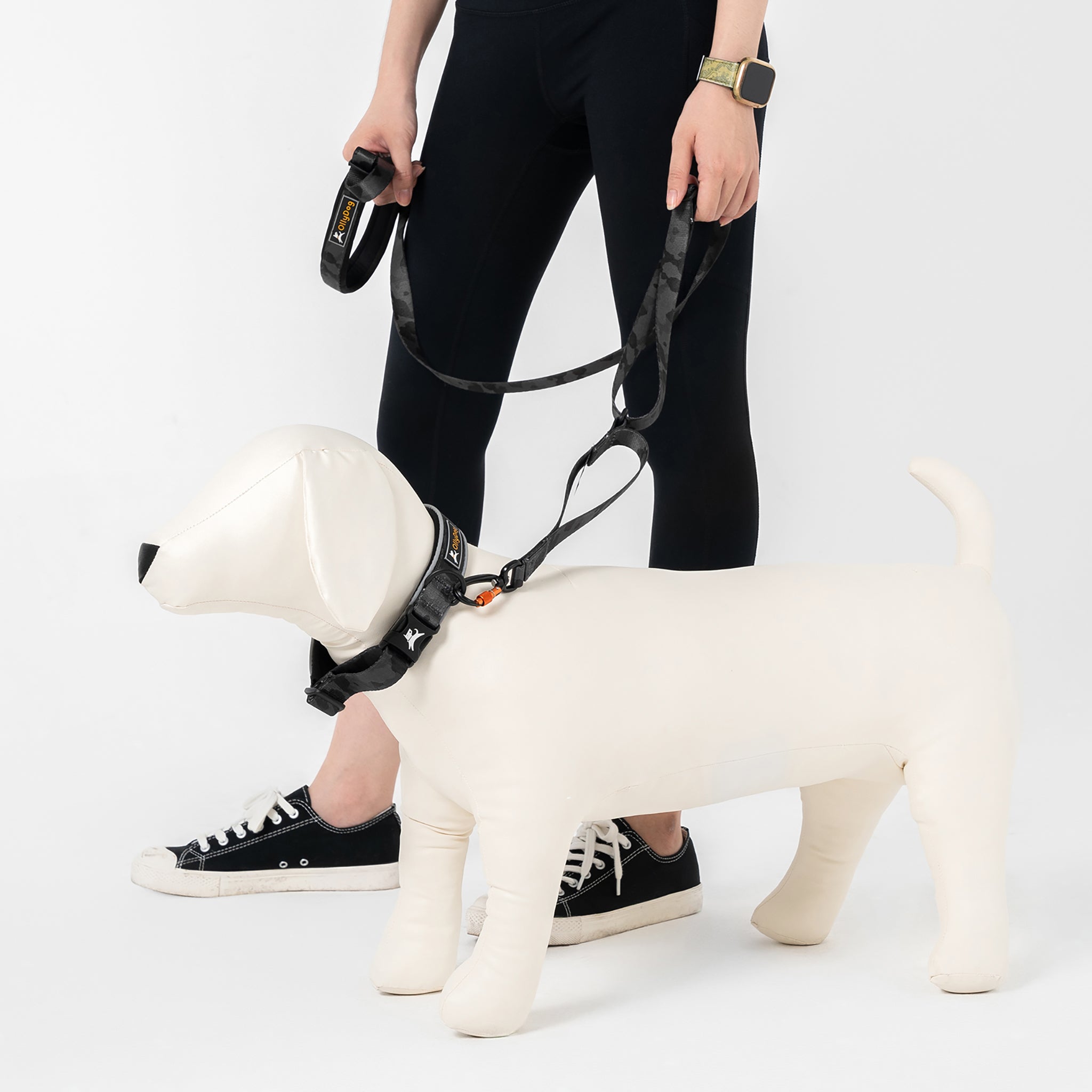Person holding the OllyDog Flagstaff Adjustable Leash in Dream Camo, attached to a dog mannequin. The leash displays its padded handle, adjustable waist belt, durable polyester webbing, and swivel carabiner, ideal for hands-free dog walking and training #color_dream camo