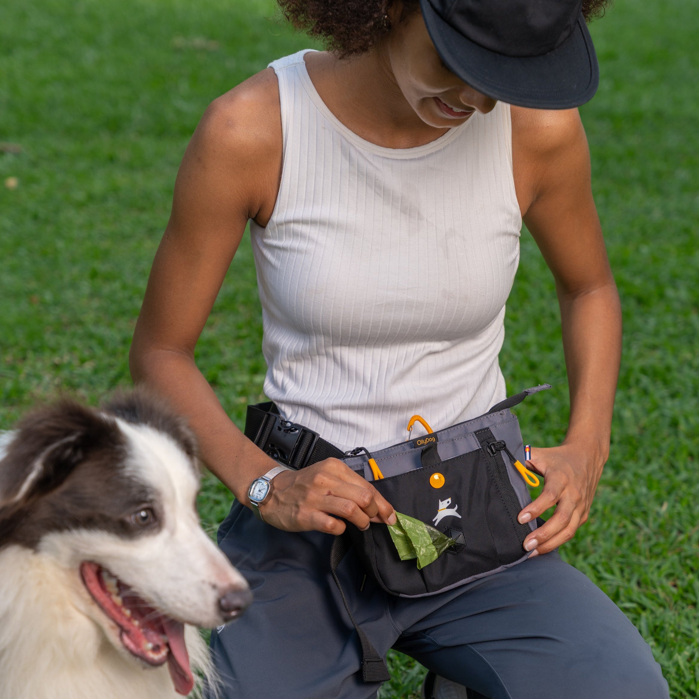 Woman using the OllyDog Backcountry Day Bag in Castle Rock during a dog walk, pulling out a waste bag with her dog nearby #color_castle rock