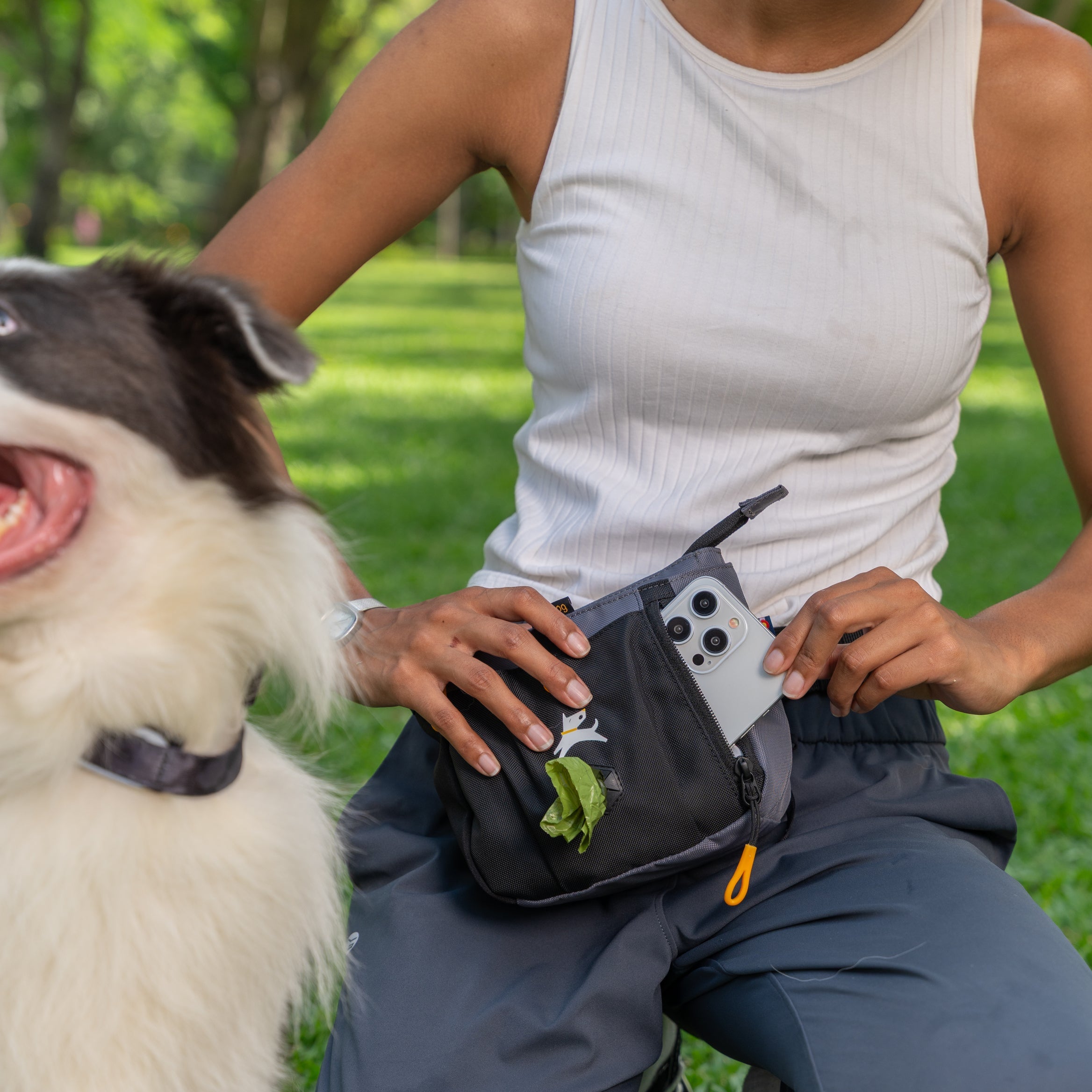 Woman using the OllyDog Backcountry Day Bag in Castle Rock during a dog walk, storing a smartphone in the front pocket with a dog beside her #color_castle rock