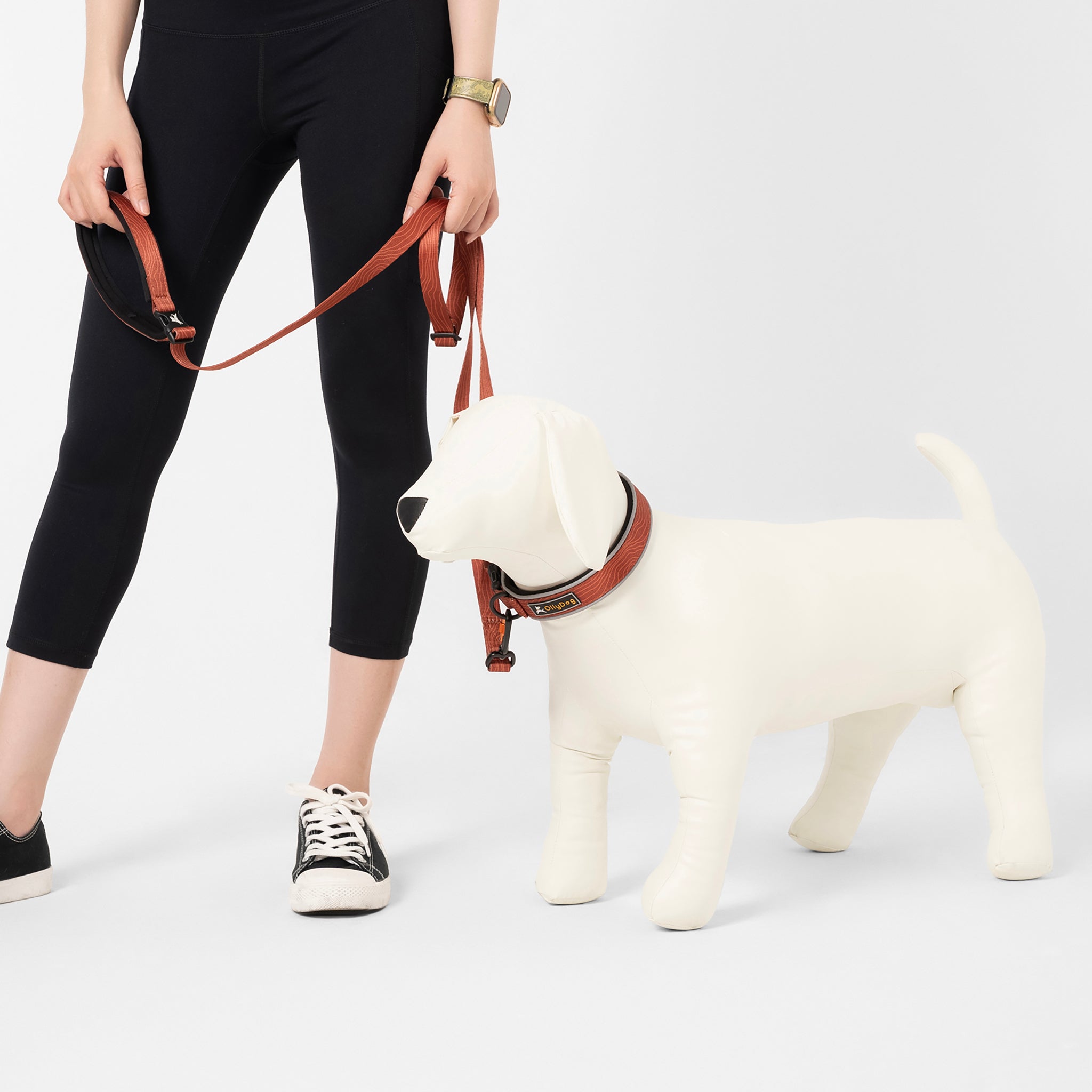 Person holding the OllyDog Flagstaff Adjustable Leash in Clay Woodgrain color, clipped to a mannequin dog wearing a matching collar. The leash shows its adjustable length and padded handle, ideal for versatile walking setups #color_clay woodgrain