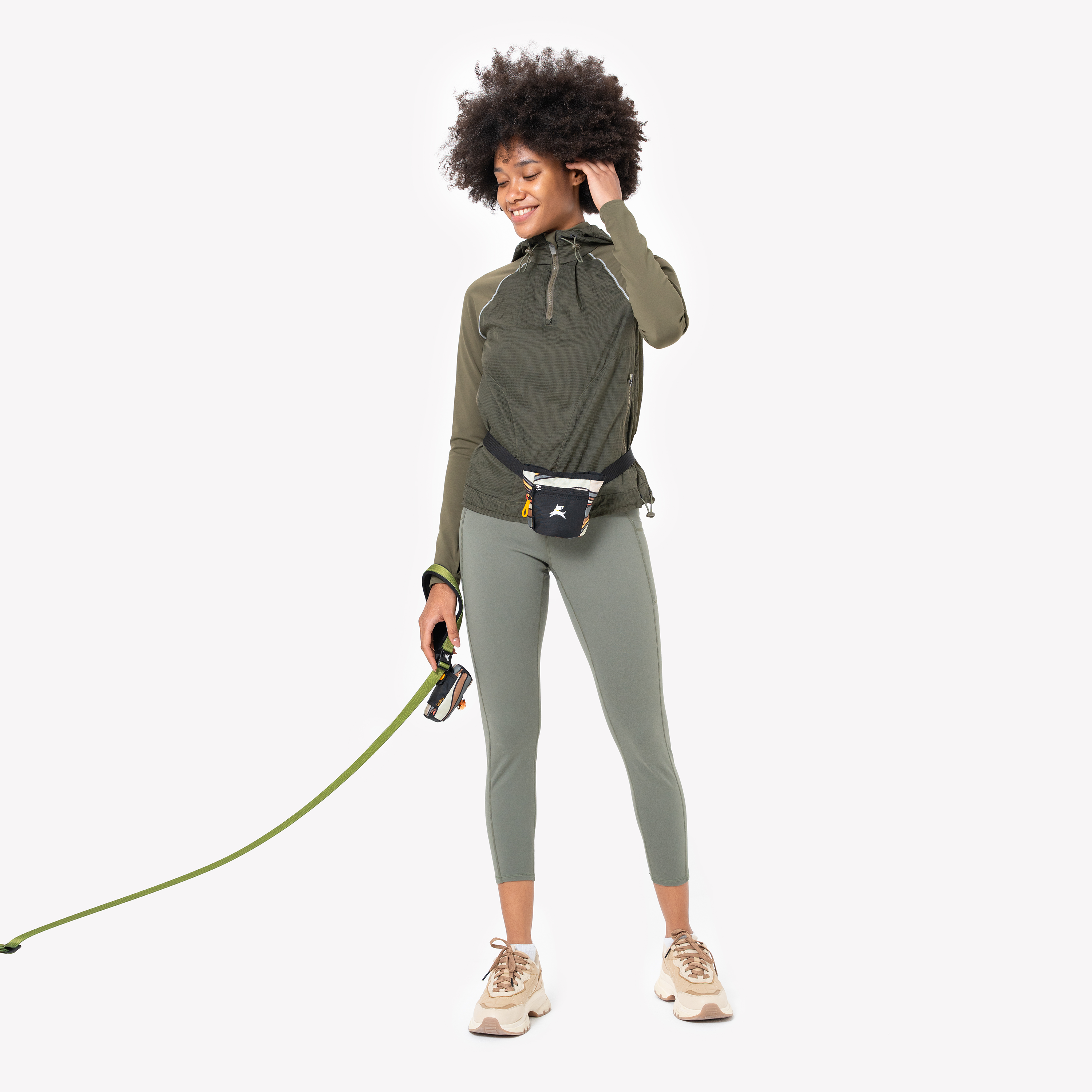 A person with dark curly hair wearing a ventura '73 OllyDog Goodie Treat Bag around their waist, holding a dog leash in their left hand, demonstrating easy access during a walk #color_ventura '73