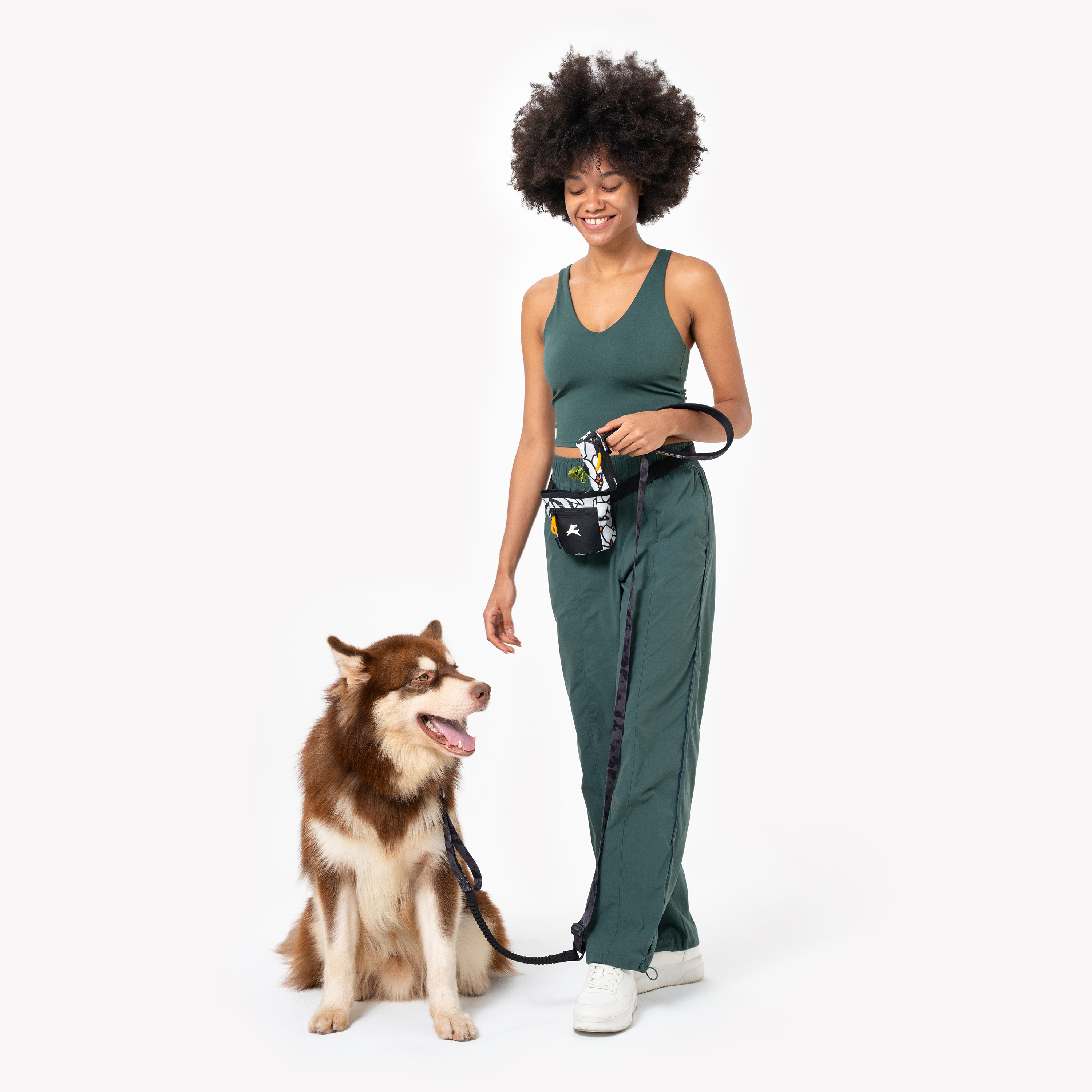 Woman walking a brown and white dog while wearing the OllyDog Goodie Treat Pouch in Magnolia color clipped to her waist #color_magnolia