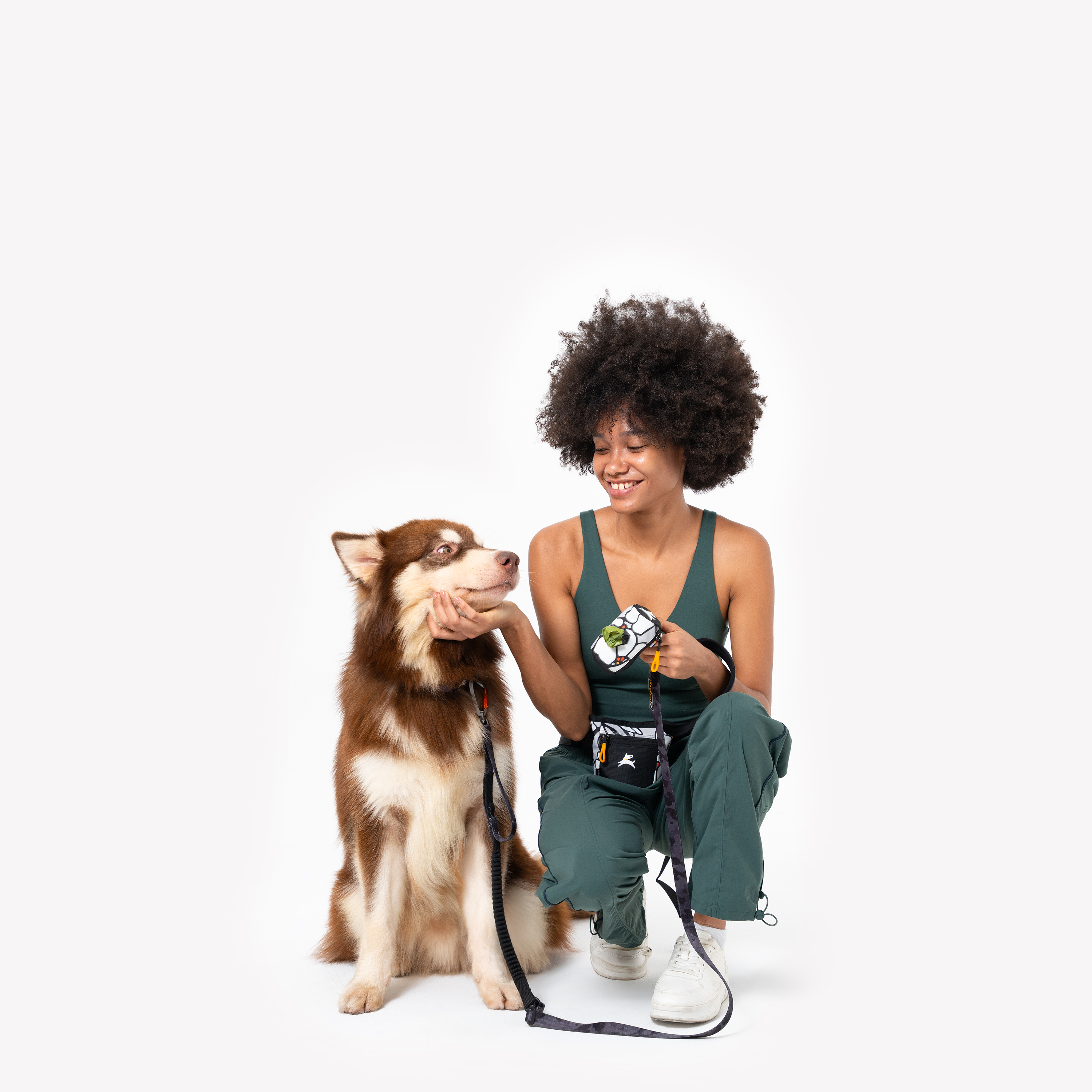 Woman sitting and smiling at a brown and white dog while holding the OllyDog Goodie Treat Pouch in Magnolia color #color_magnolia