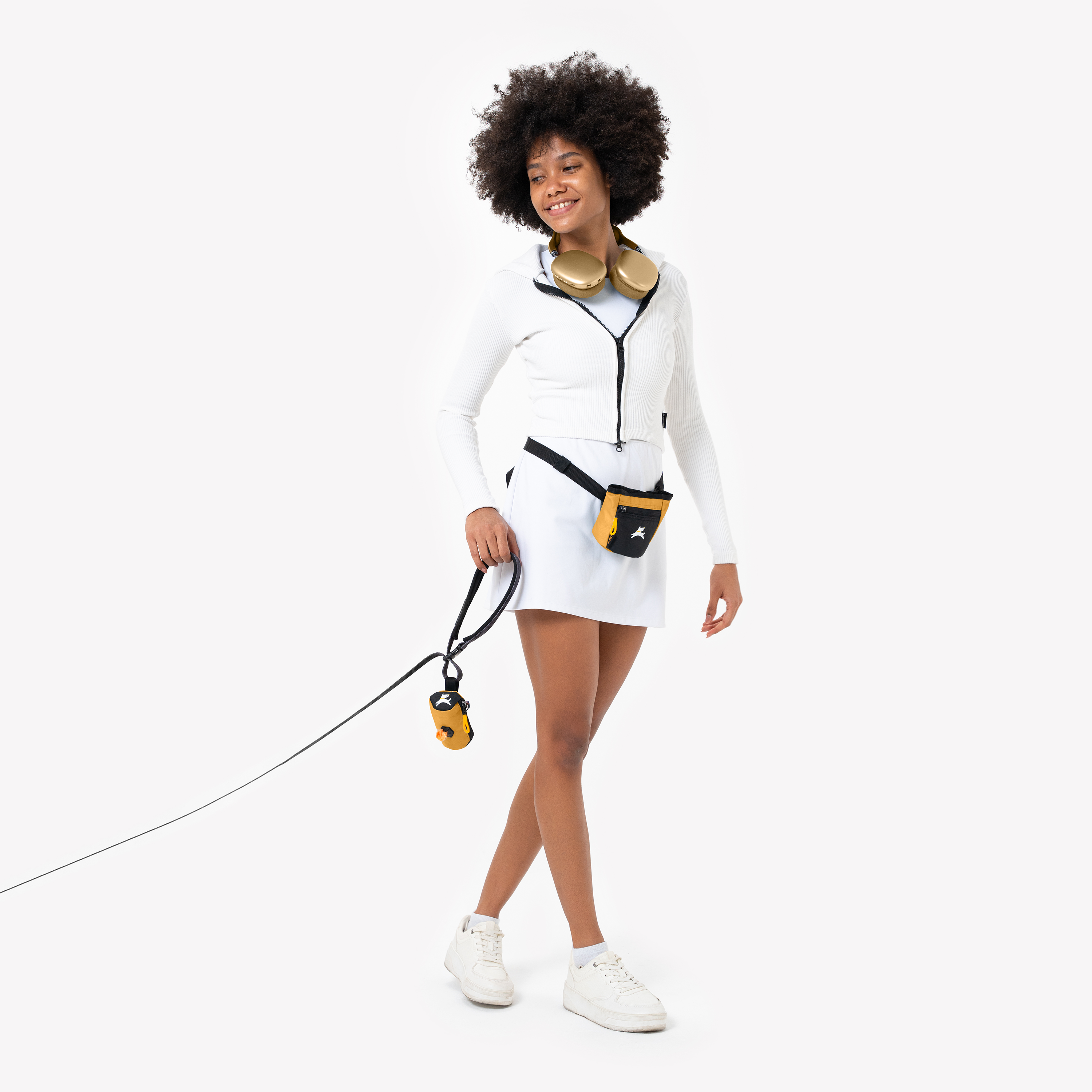 Stylish woman walking dog with yellow treat pouch and waste bag dispenser, wearing white activewear and headphones #color_sundial