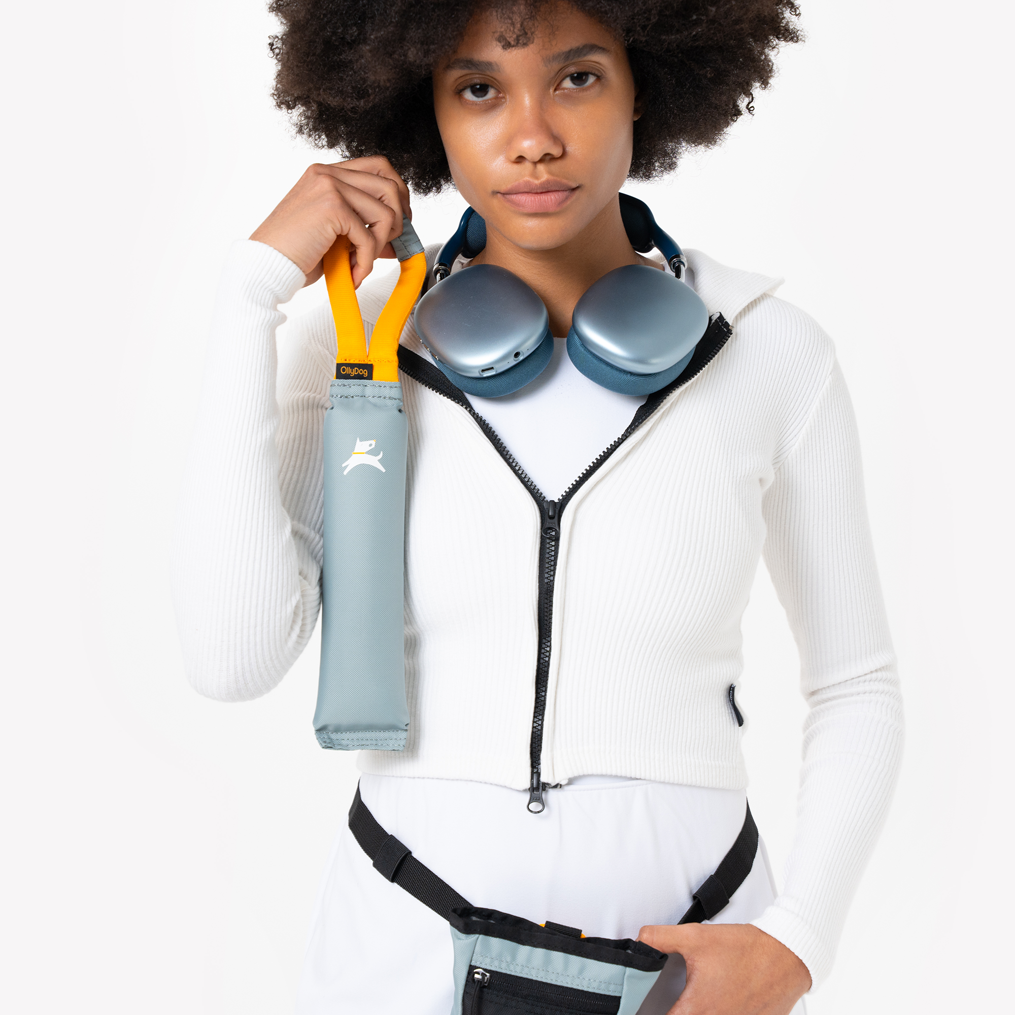 Person holding the OllyDog Tugger dog toy in St. Lucia color by the sturdy yellow handle. The recycled, non-toxic tug toy is designed for interactive play, tugging, and fetching, shown with a matching waist pack #color_st. lucia