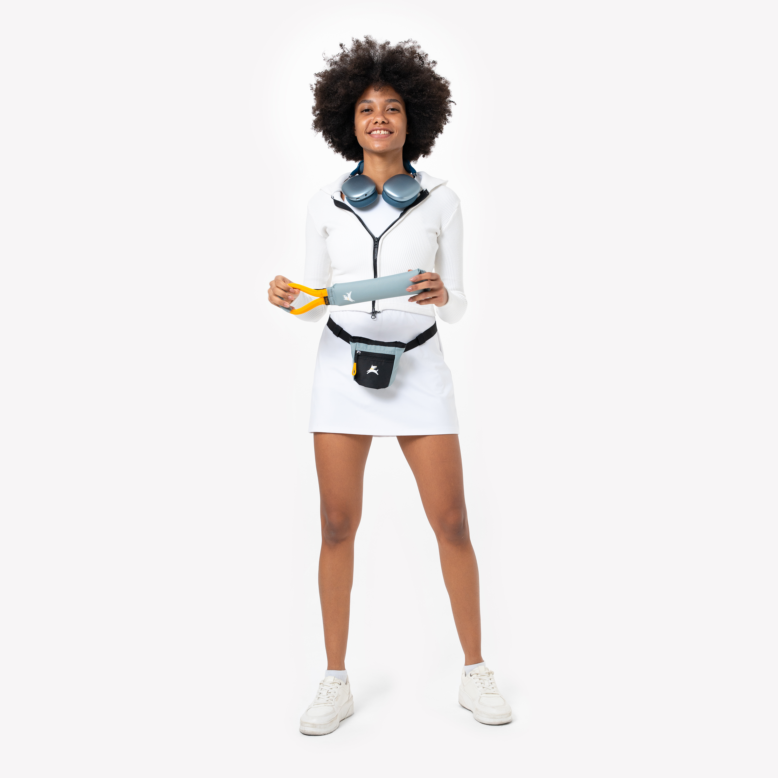 Person standing and holding the OllyDog Tugger dog toy in St. Lucia color, featuring a recycled, non-toxic design with a yellow handle. The toy is made for tugging and fetching, shown with a matching waist pack for dog walking #color_st. lucia