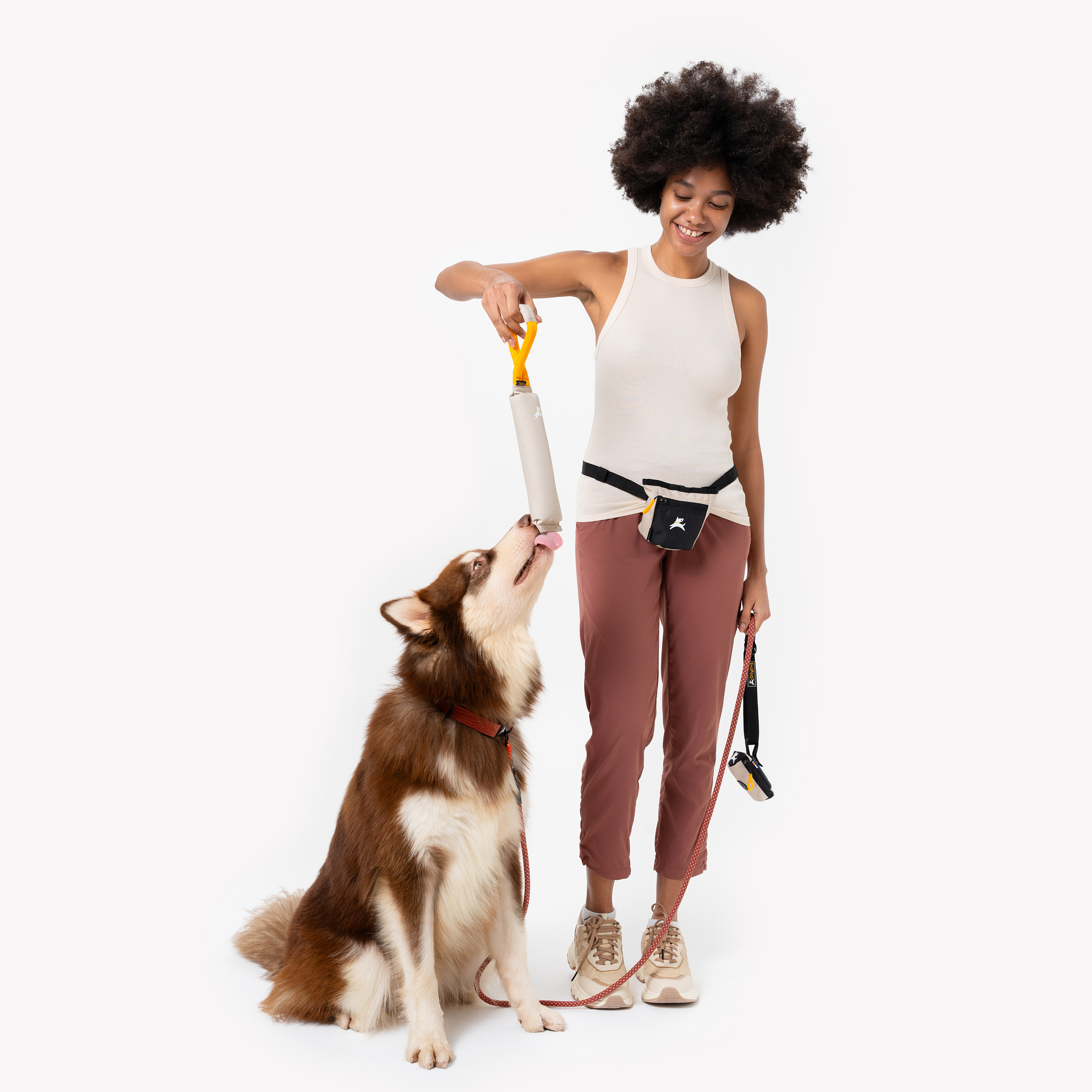 Person playing with a dog using the OllyDog Tugger toy in Con Leche color. The dog is tugging on the sturdy yellow handle of the recycled, non-toxic toy, designed for interactive play, fetch, and chewing #color_con leche