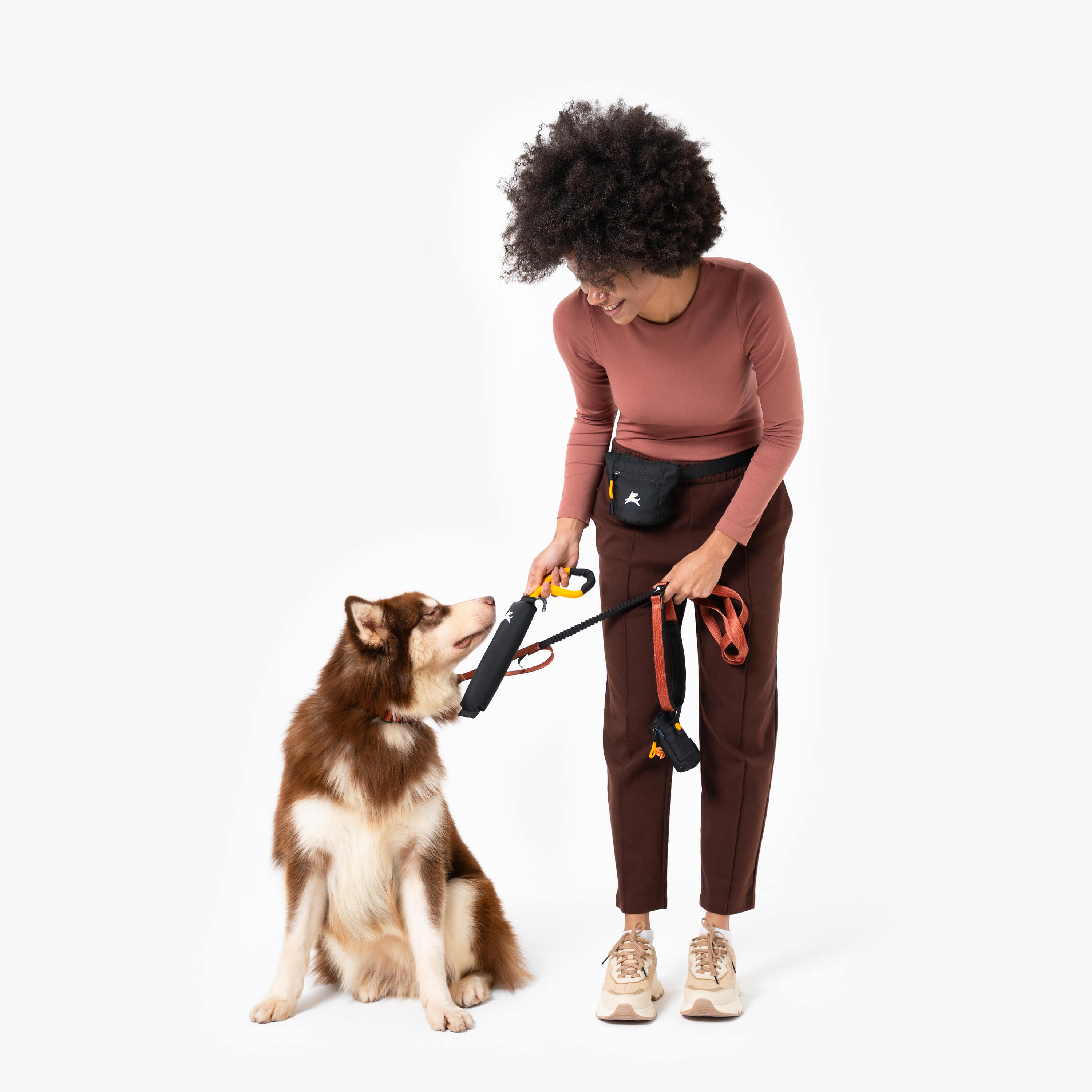 Trainer interacts with a Husky using the OllyDog Tugger interactive dog toy in Raven colorway. The black tug toy with a yellow handle is held out as the dog focuses intently, both standing against a white background #color_raven