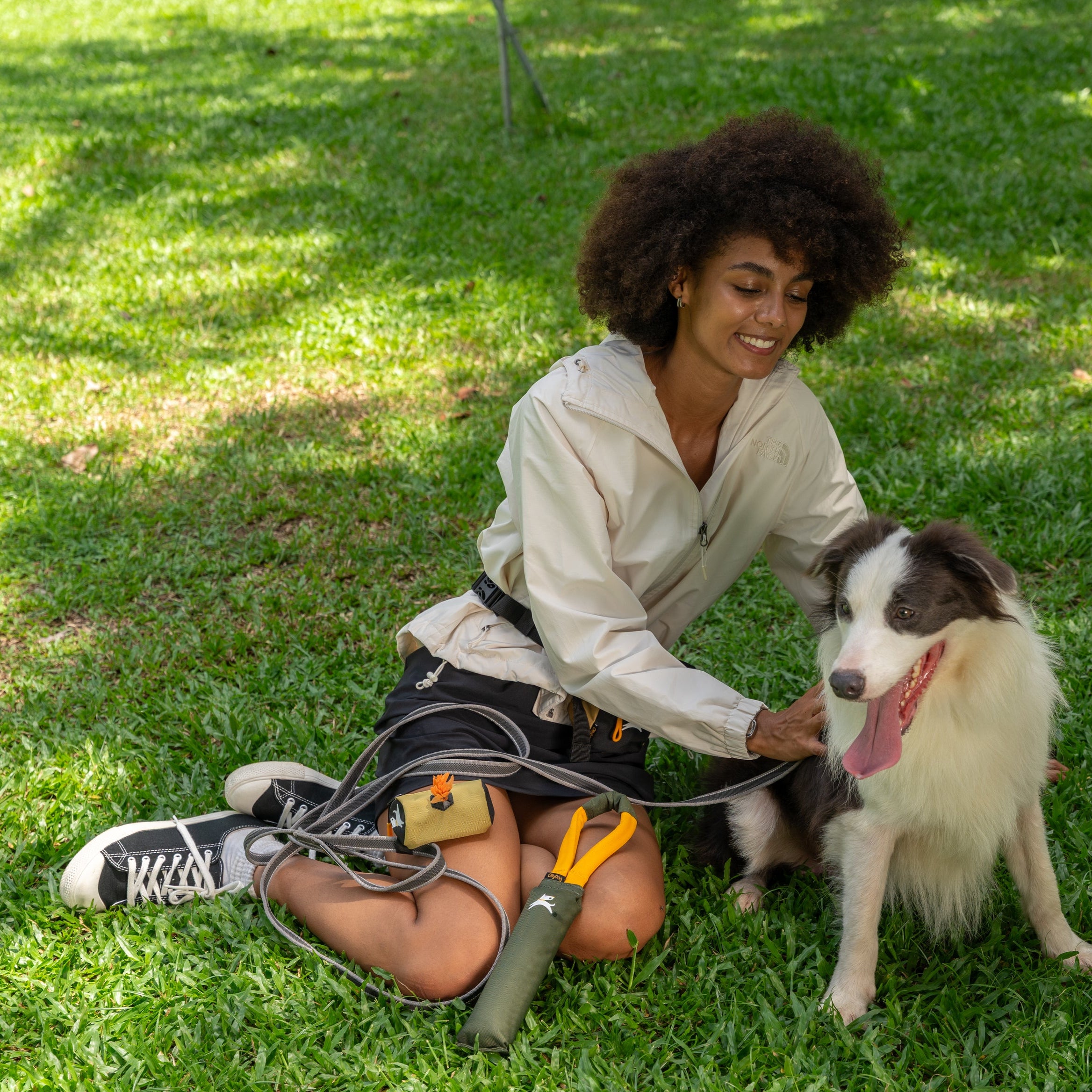Woman kneeling on grass petting her dog with the OllyDog Scoop Pick Up Bag in Alchemy color clipped to the leash #color_alchemy