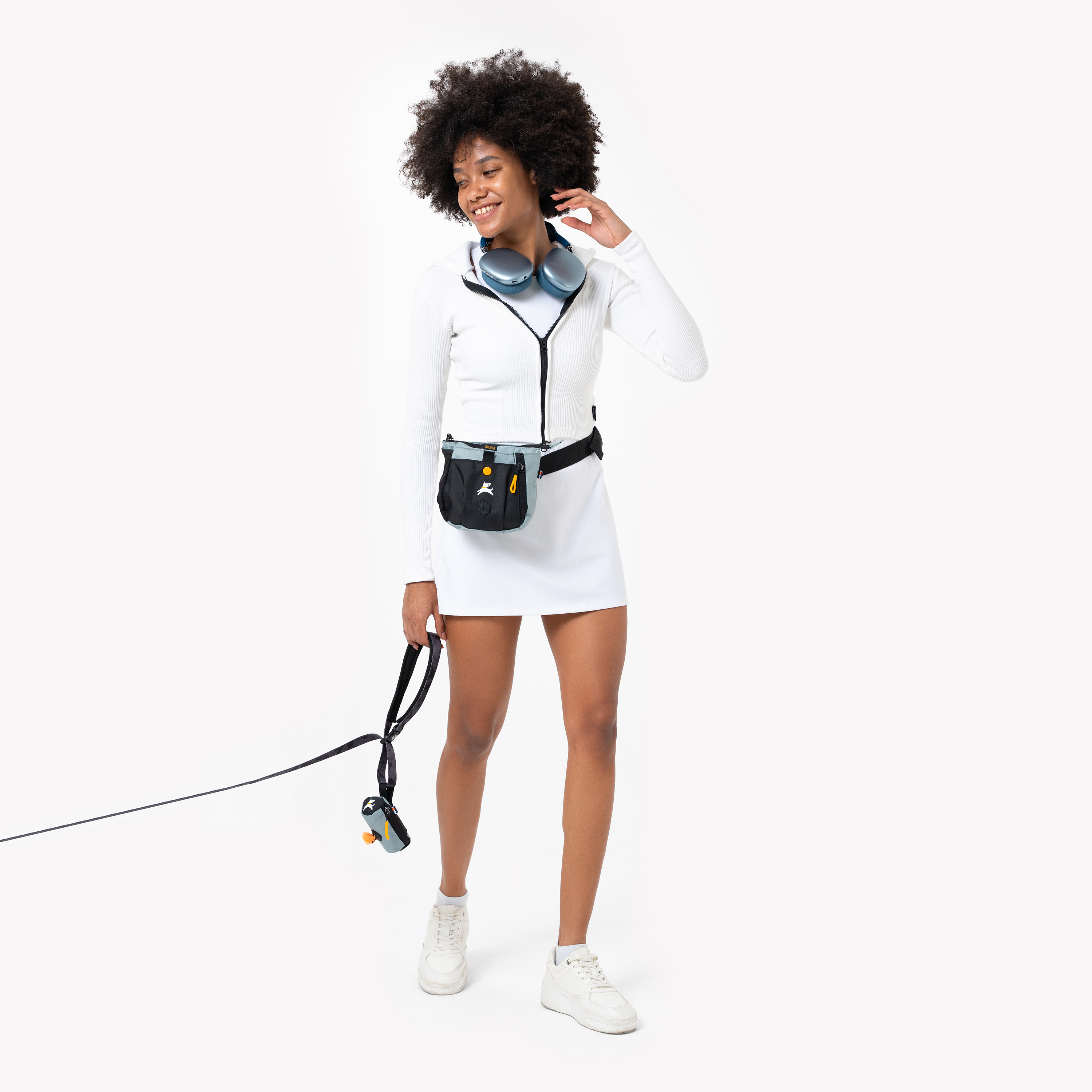 Woman walking a dog with Scoop Pick Up Bag attached to the leash and wearing a treat pouch around her waist, dressed in white athletic wear with headphones around her neck #color_st. lucia