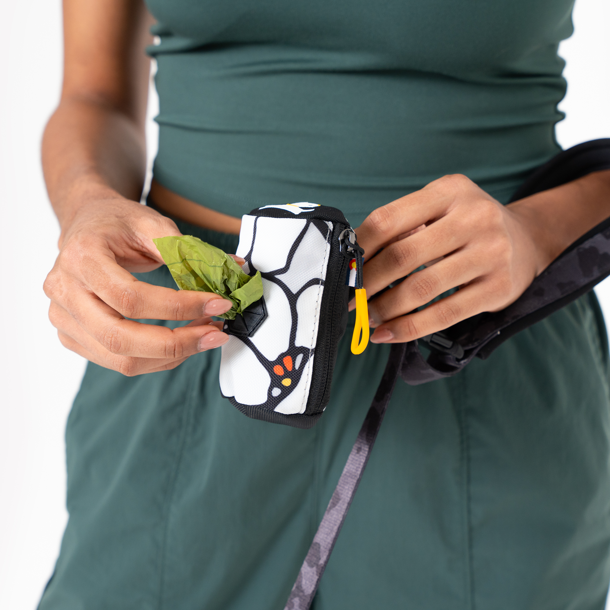 Person pulling a green waste bag from a patterned Scoop Pick Up Bag with zipper closure and front dispenser, attached to a leash #color_magnolia