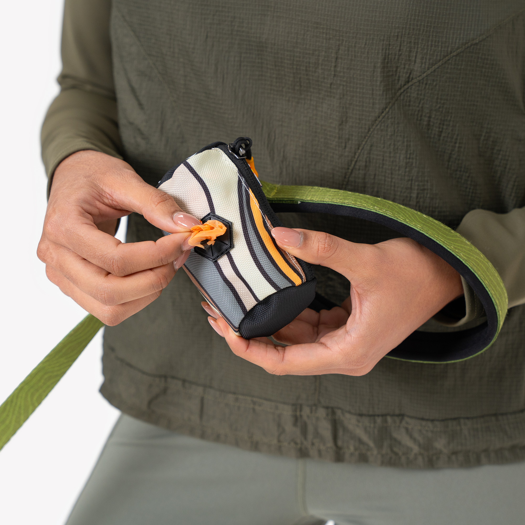 Person pulling an orange waste bag from a striped Scoop Pick Up Bag with zipper closure and dispenser, attached to a green leash. #color_ventura '73