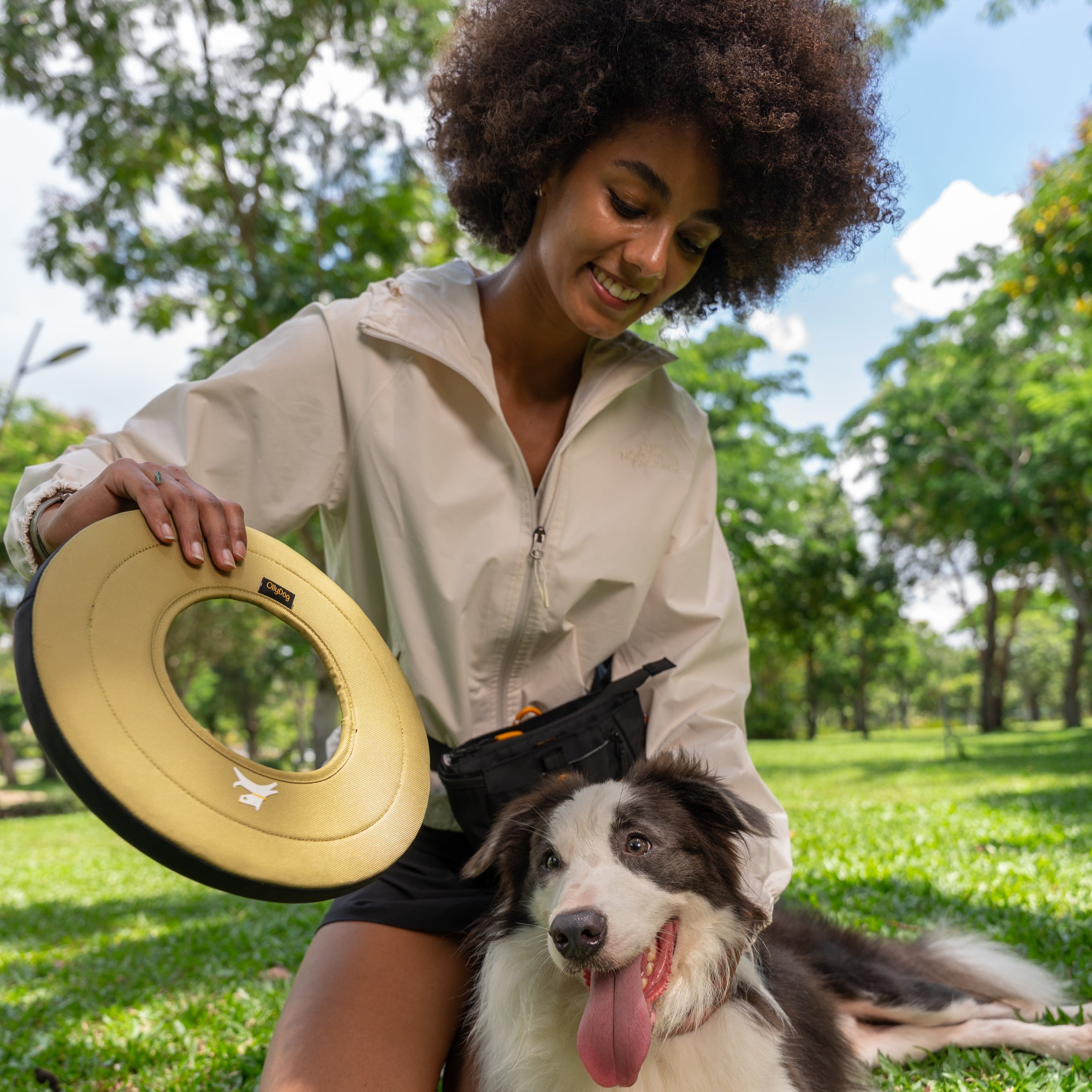 Woman holding the OllyDog Super Flyer in Alchemy color while smiling at her dog in a sunny park setting #color_alchemy