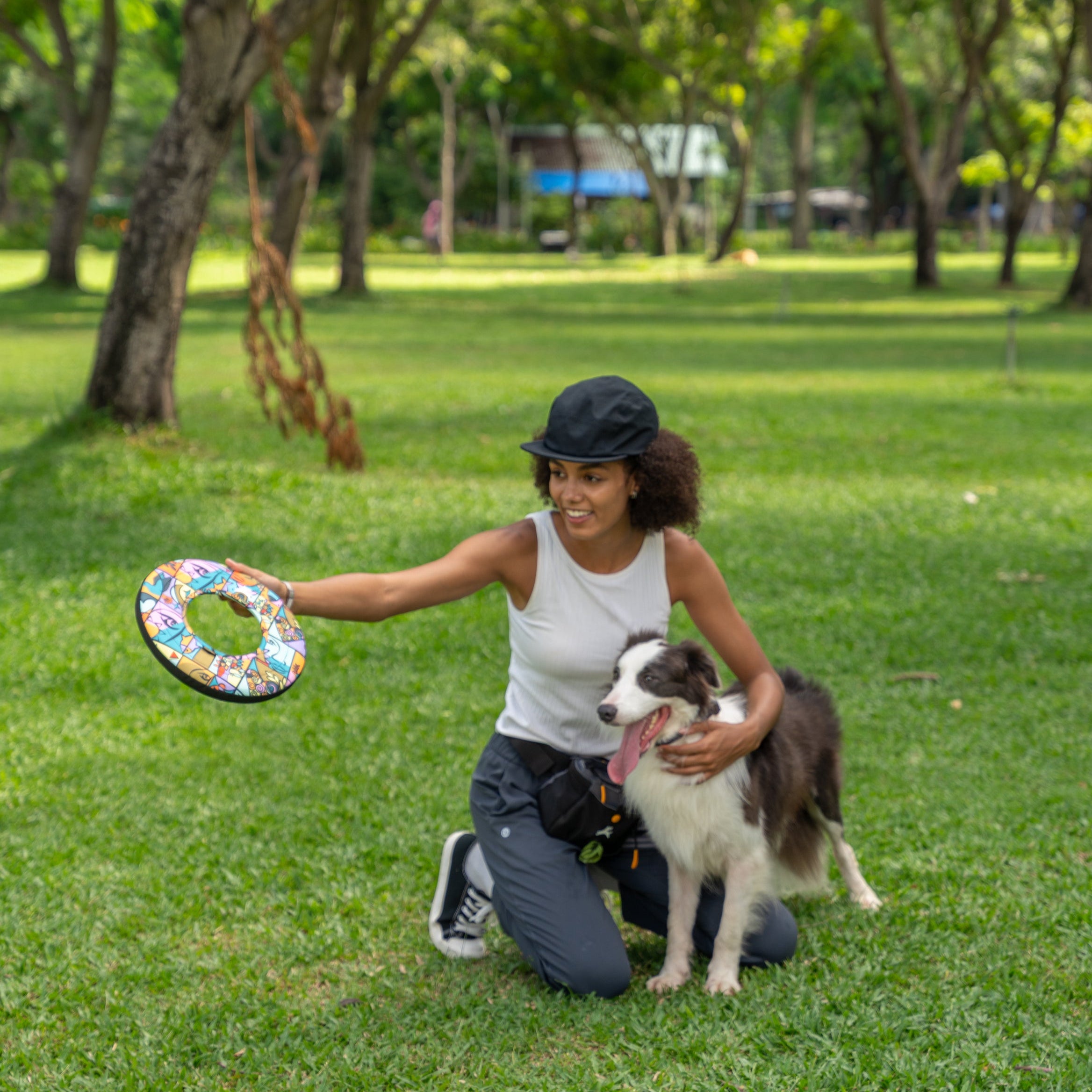 Woman kneeling in the park holding the OllyDog Super Flyer in Cloud9 pattern, preparing to play fetch with her happy dog #color_cloud9