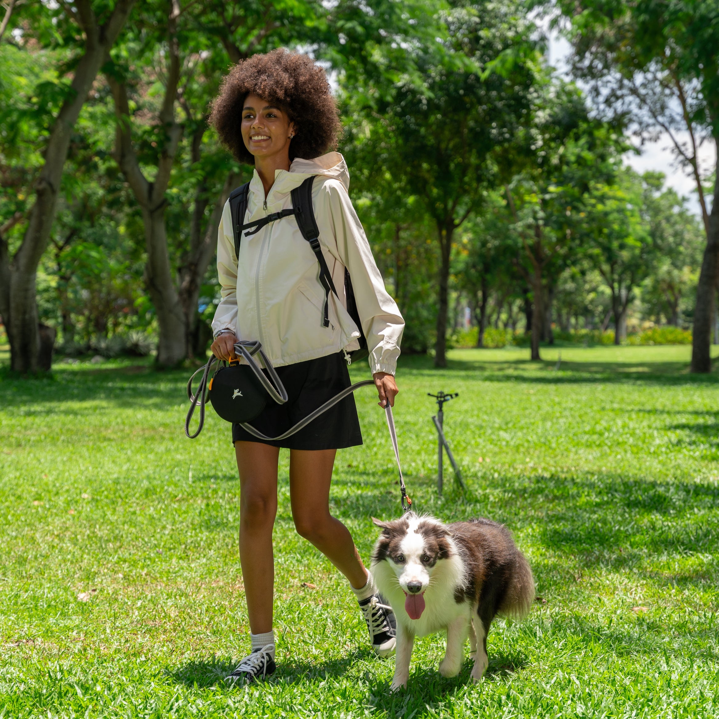 Woman walking her dog in the park with the OllyDog Superbowl in Winter Moss color clipped to her waist in folded compact form #color_winter moss