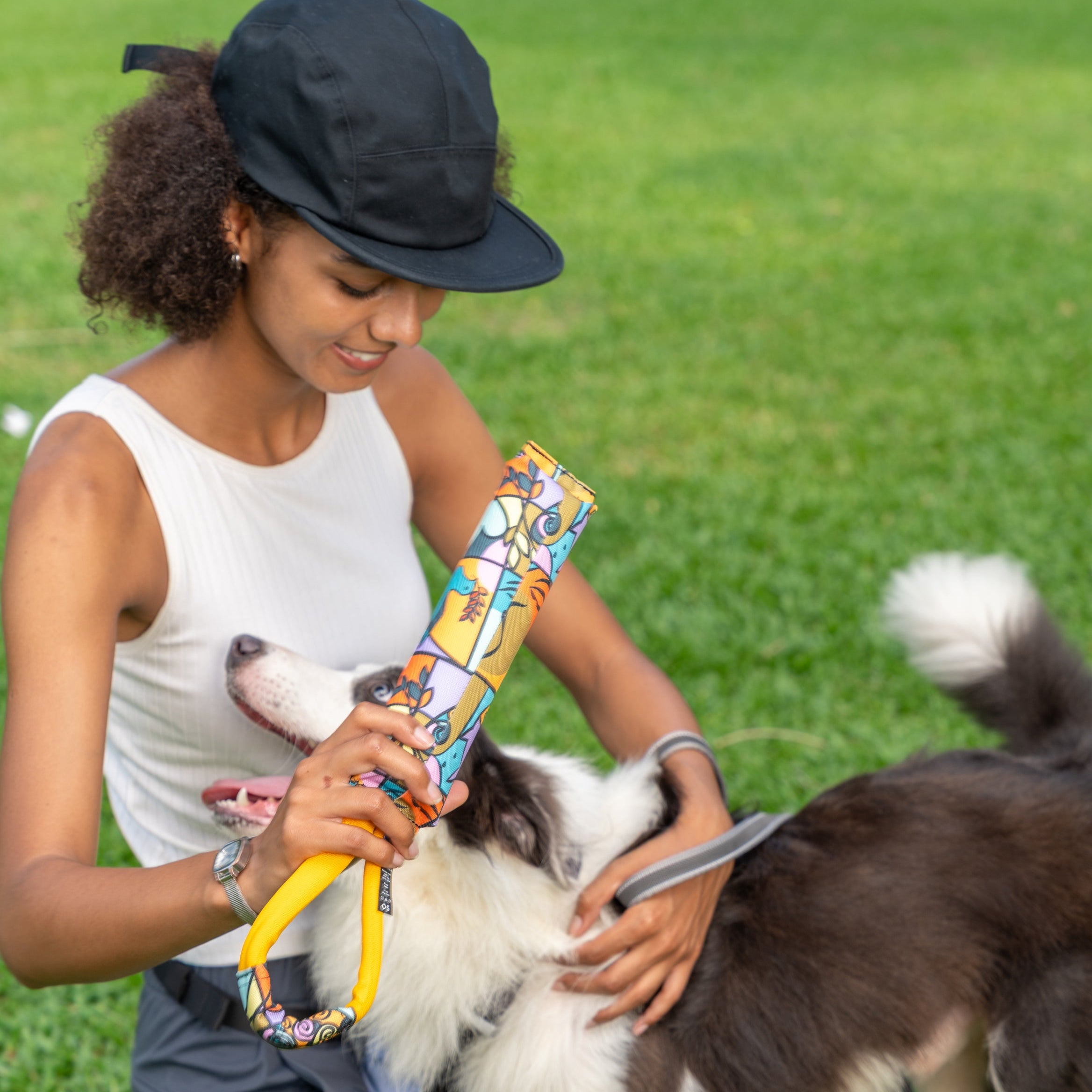 Woman smiling and holding the OllyDog Tugger Toy in Cloud9 pattern while playing with her excited dog in the park #color_cloud9