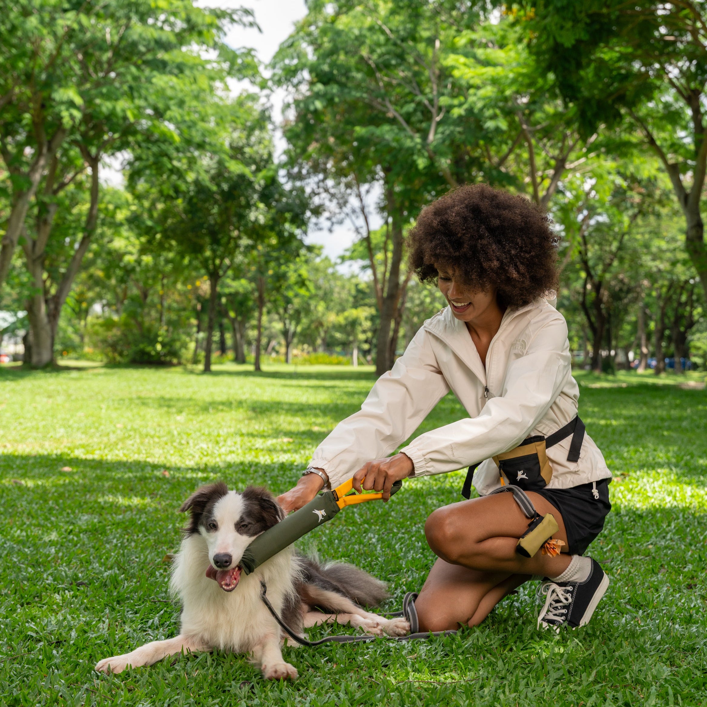 Woman tugging with her dog in the park using the OllyDog Tugger Toy in Winter Moss color, designed from recycled materials with a yellow handle #color_winter moss