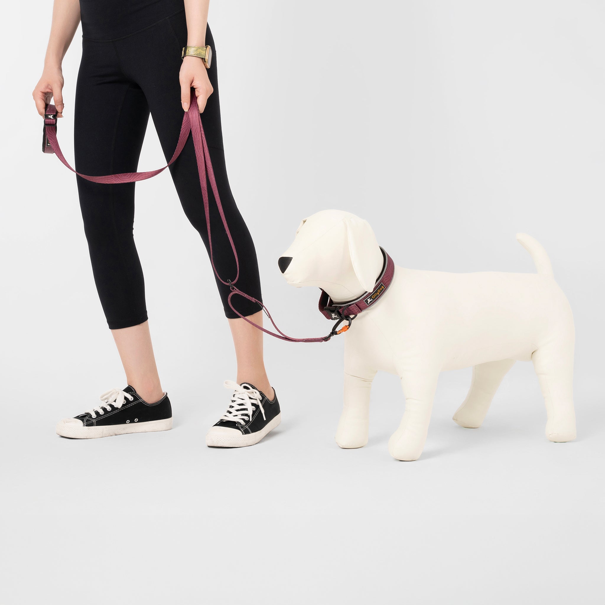 Person holding the OllyDog Flagstaff Adjustable Leash in Rosewood Woodgrain color, attached to a white mannequin dog. Leash shown in adjustable length with padded handle and swivel carabiner clip #color_rosewood woodgrain