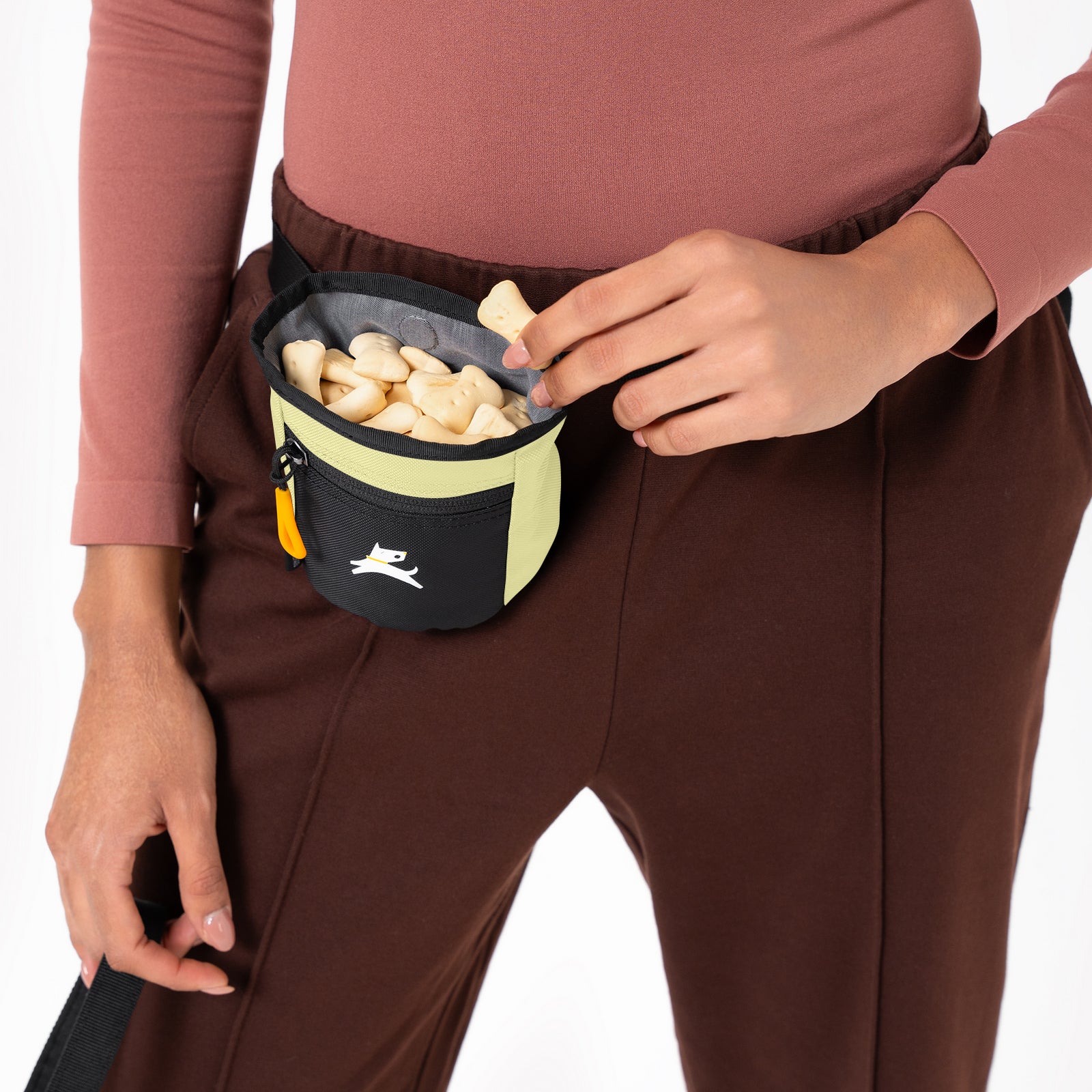 Close-up of a person wearing the OllyDog Goodie Treat Bag in sol color around their waist and reaching inside for a dog training treat. #color_sol