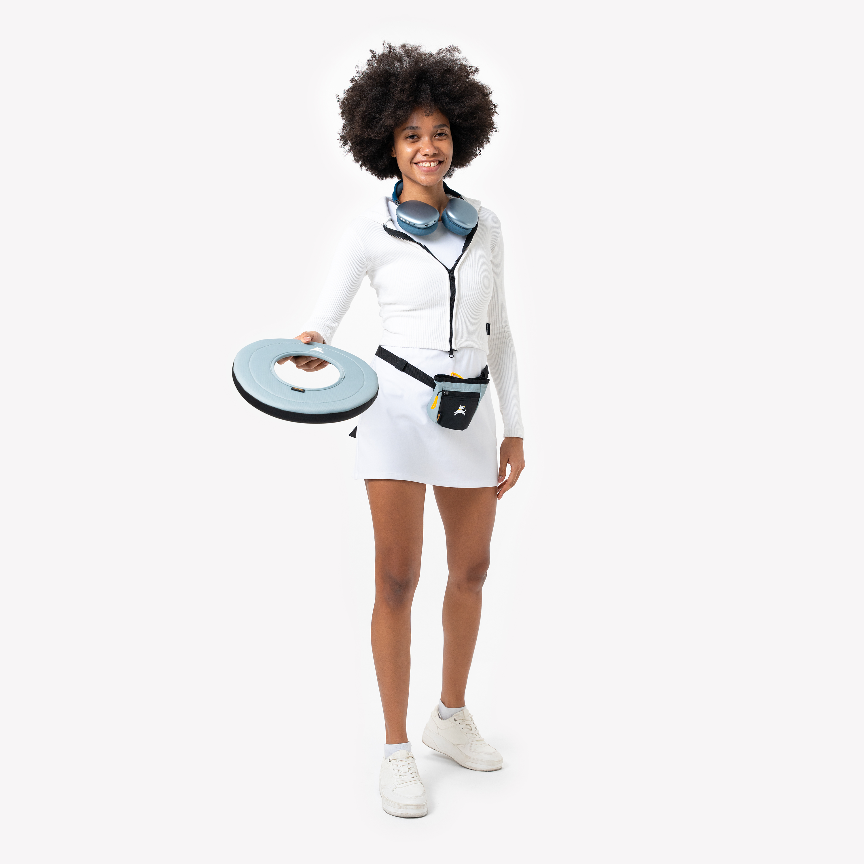 Woman in white activewear holding a St. Lucia SuperFlyer fabric dog frisbee, with treat pouch worn at waist, ready for outdoor fetch play #color_st. lucia