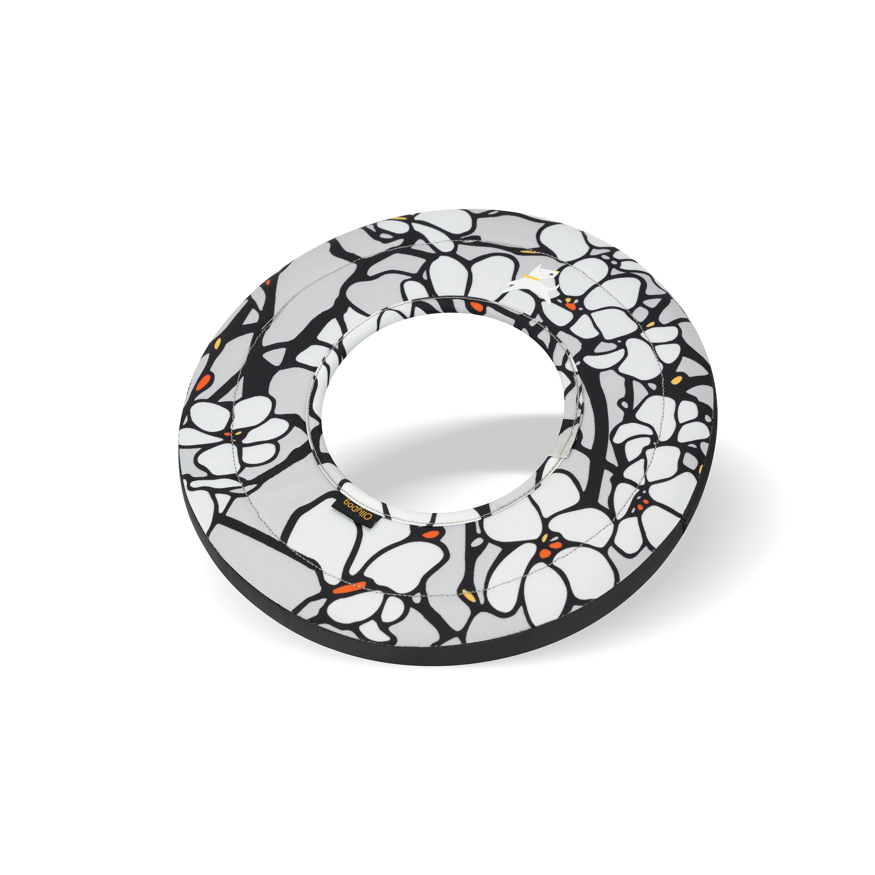 Side view of Magnolia Super Flyer dog frisbee showing soft ring structure and bold floral pattern in black, white, and orange accents with visible shadow for dimension #color_magnolia
