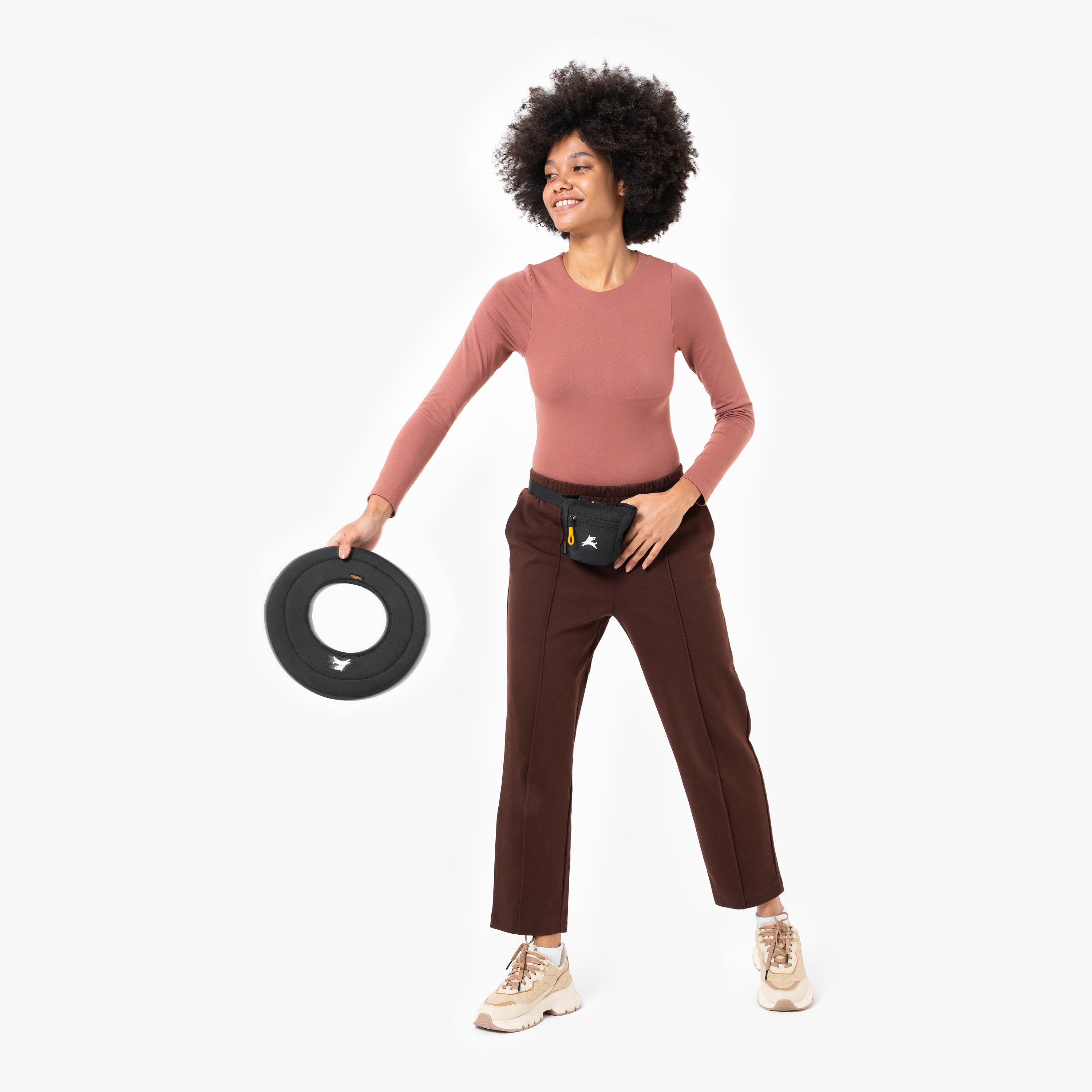 Woman wearing a mauve top and dark pants, playfully holding the OllyDog Super Flyer fabric dog frisbee in Raven black #color_raven
