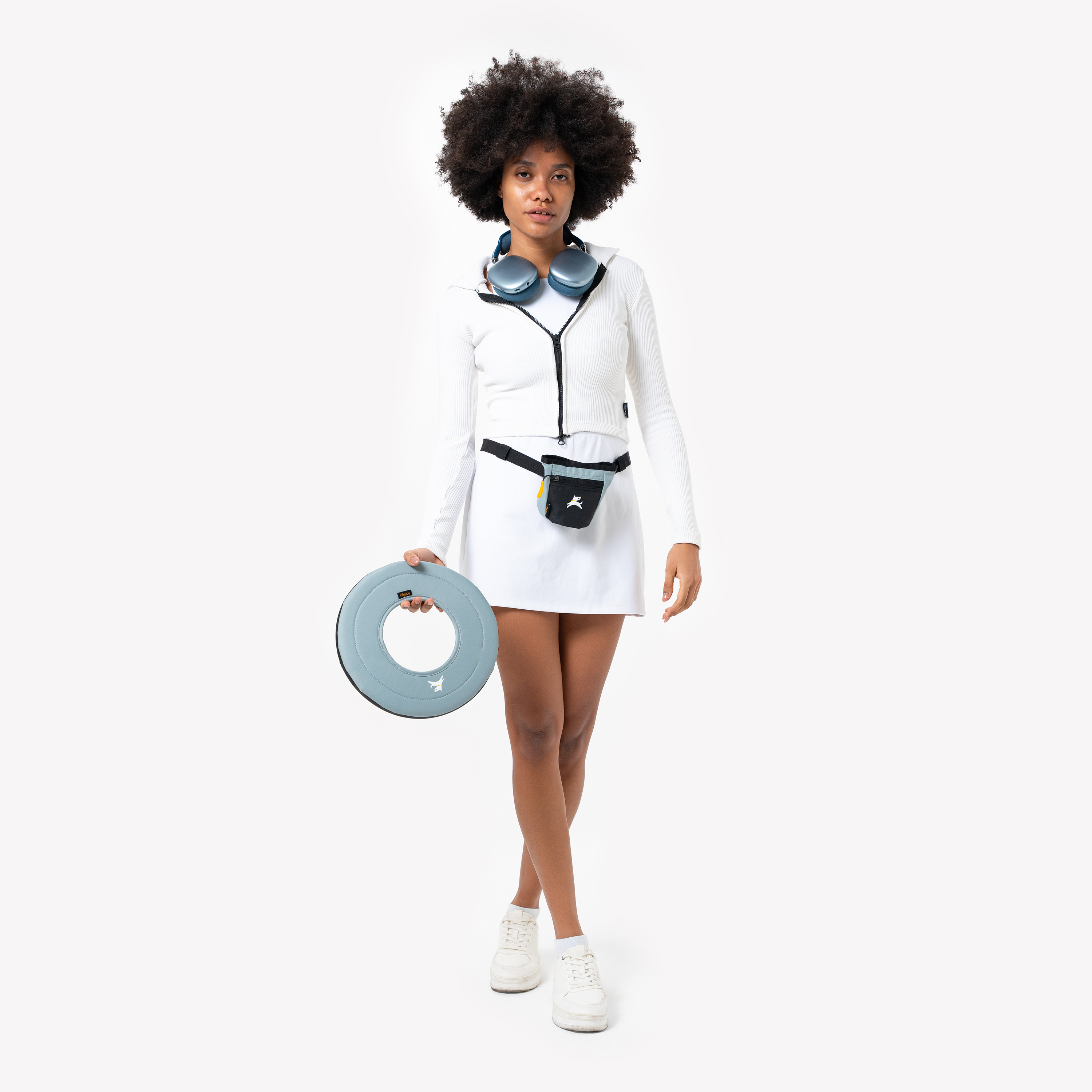 Woman in white athletic outfit holding a St. Lucia Super Flyer fabric dog frisbee, with treat pouch at waist, ready for fetch play or dog training #color_st. lucia