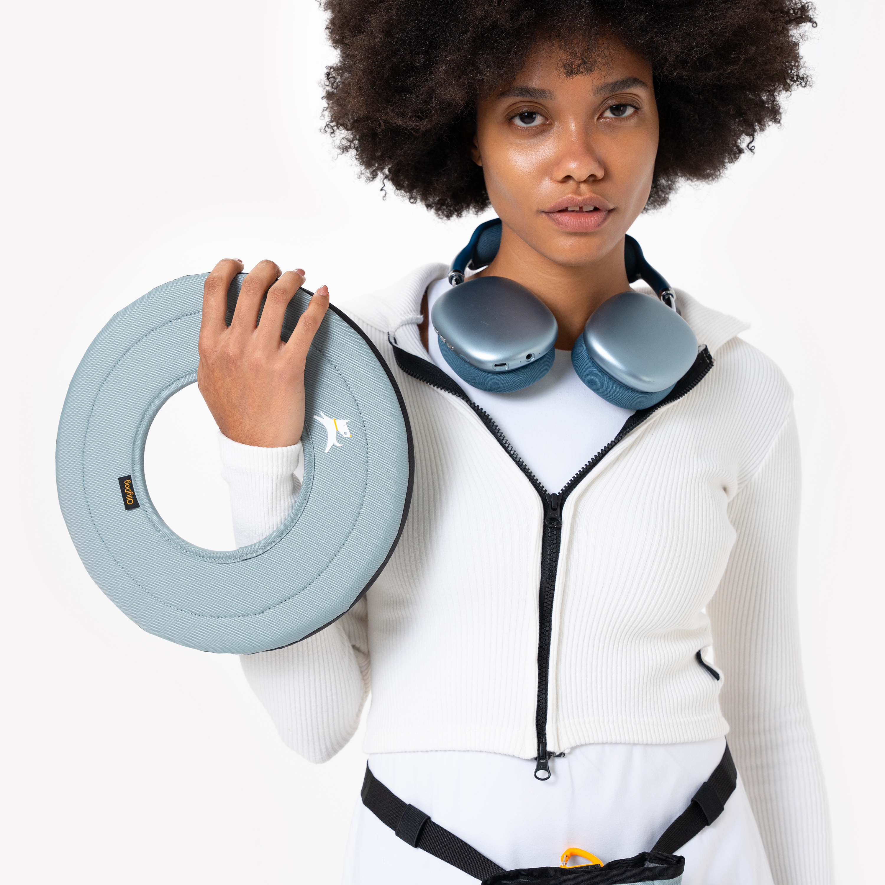Close-up of woman in white activewear holding the St. Lucia Super Flyer fabric dog frisbee, with wireless headphones around her neck and treat pouch at waist #color_st. lucia