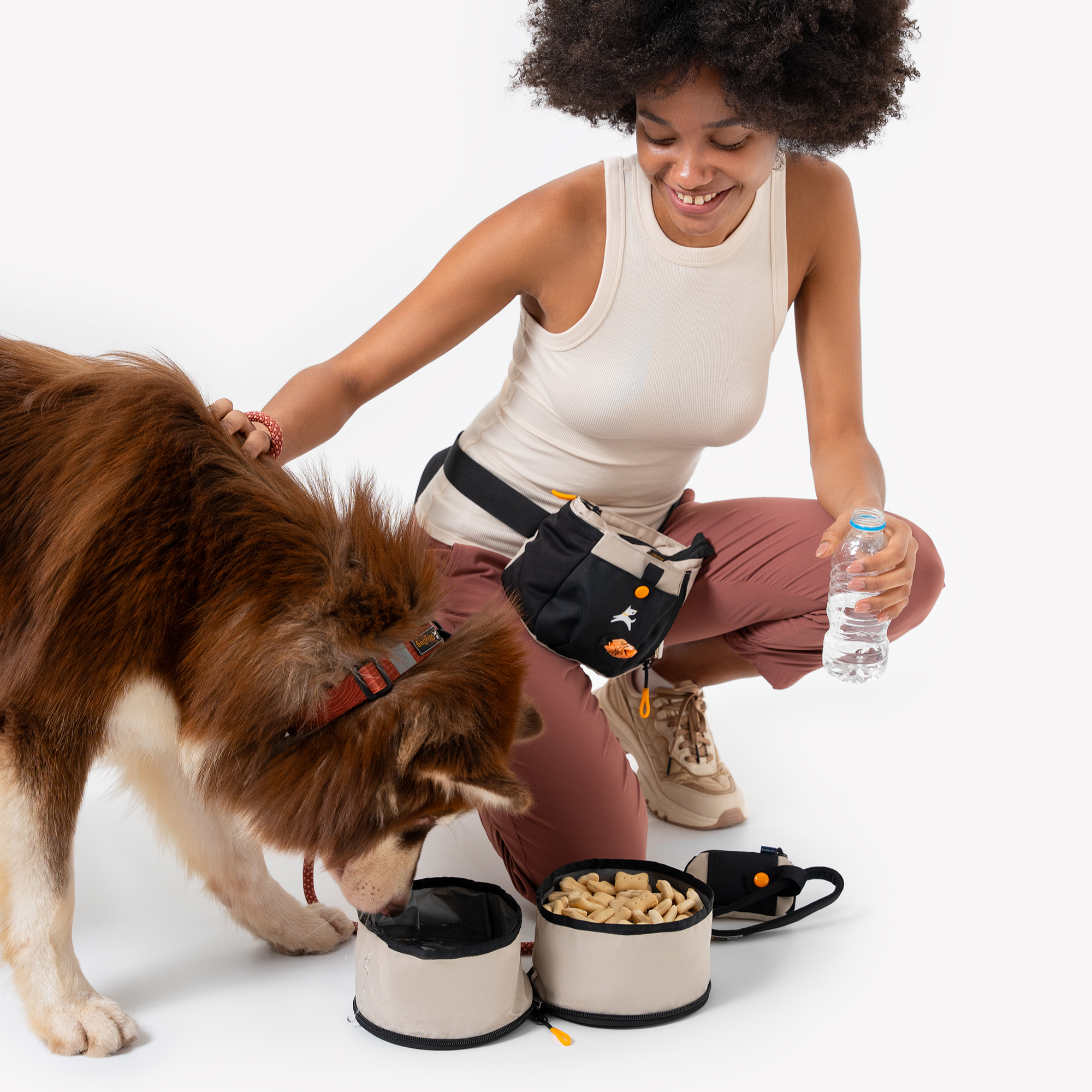Woman kneeling beside a brown dog drinking from the OllyDog Superbowl in color Con Leche, showing its two compartments filled with water and food, on a white background #color_con leche
