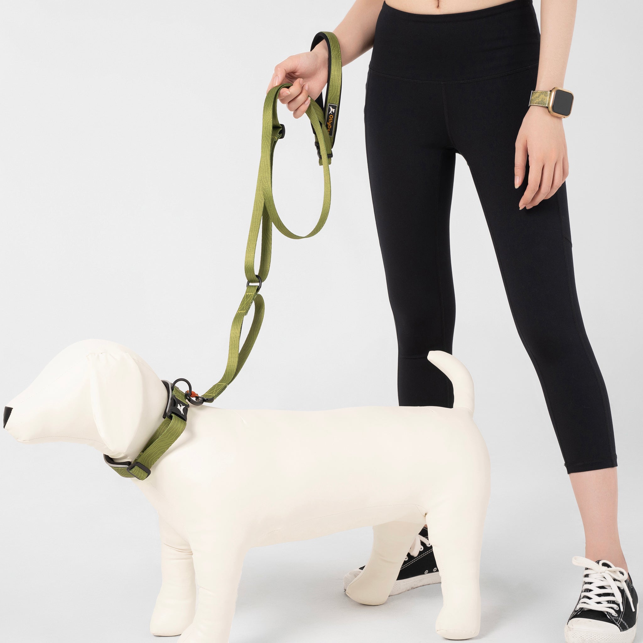 Person holding the OllyDog Flagstaff Adjustable Leash in Cactus Woodgrain, clipped to a dog mannequin. The leash showcases its padded handle, adjustable waist belt, and durable polyester webbing, designed for hands-free, secure dog walking and training #color_cactus woodgrain