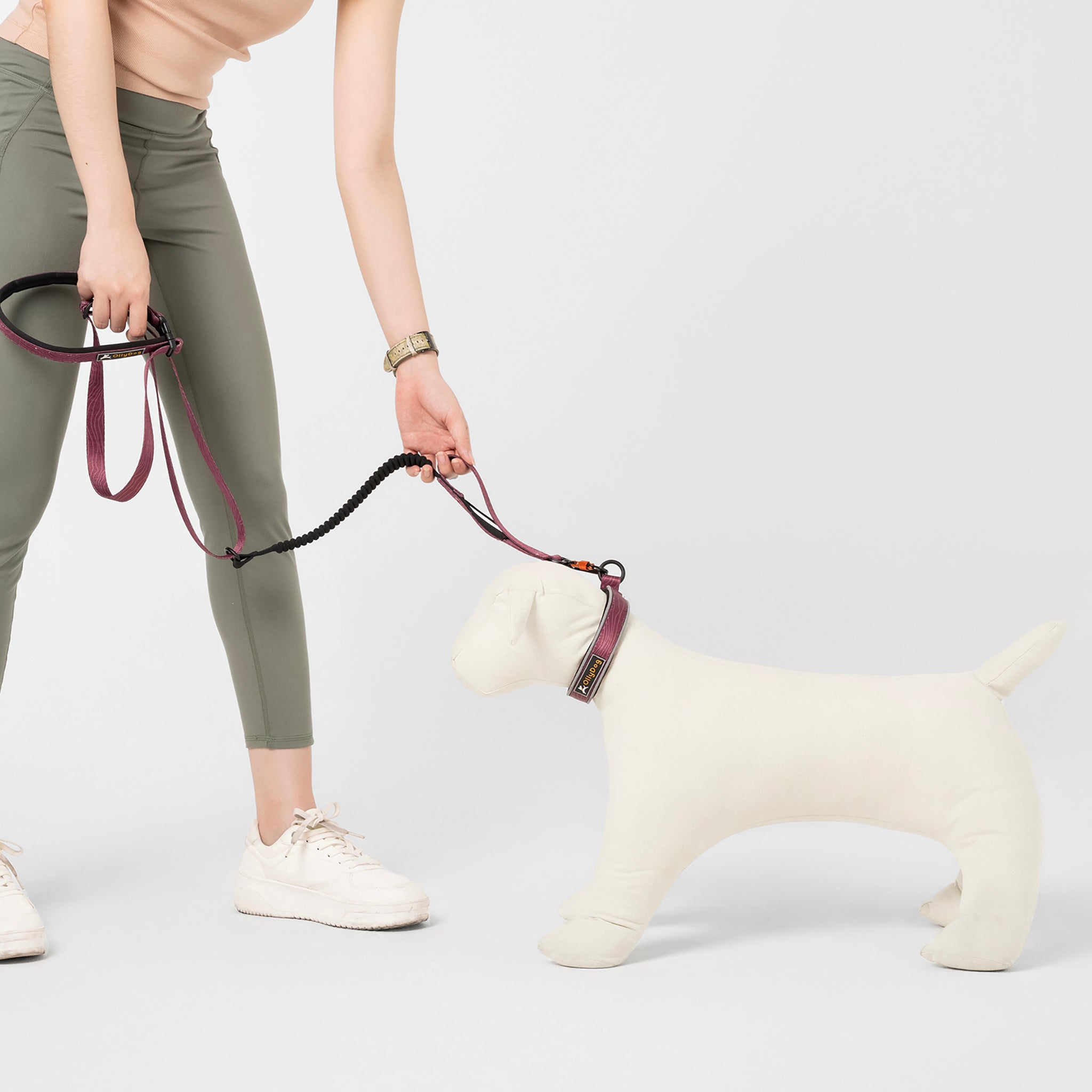 Person holding the OllyDog Flagstaff Adjustable Spring Leash in Rosewood Woodgrain, attached to a dog mannequin. The leash features a padded handle, adjustable waist belt, bungee stretch, and swivel carabiner hook, ideal for hands-free dog walking and running #color_rosewood woodgrain
