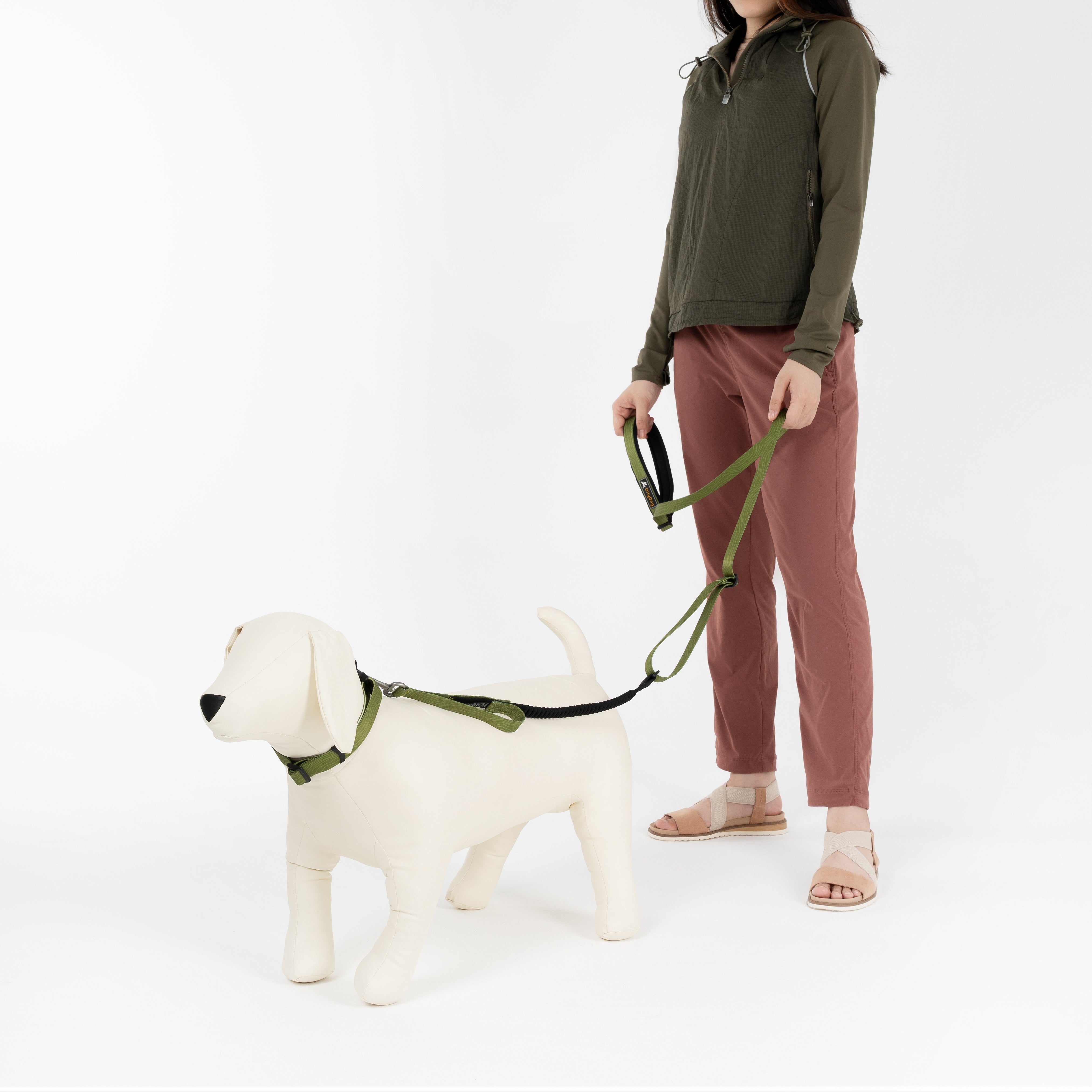 Person holding leash attached to dog mannequin wearing OllyDog Flagstaff Reflective Dog Collar and matching leash in cactus woodgrain color, showing sublimation polyester webbing, reflective band, quick-release buckle, and aluminum D-ring; durable, adjustable, and comfortable for walking #color_cactus woodgrain