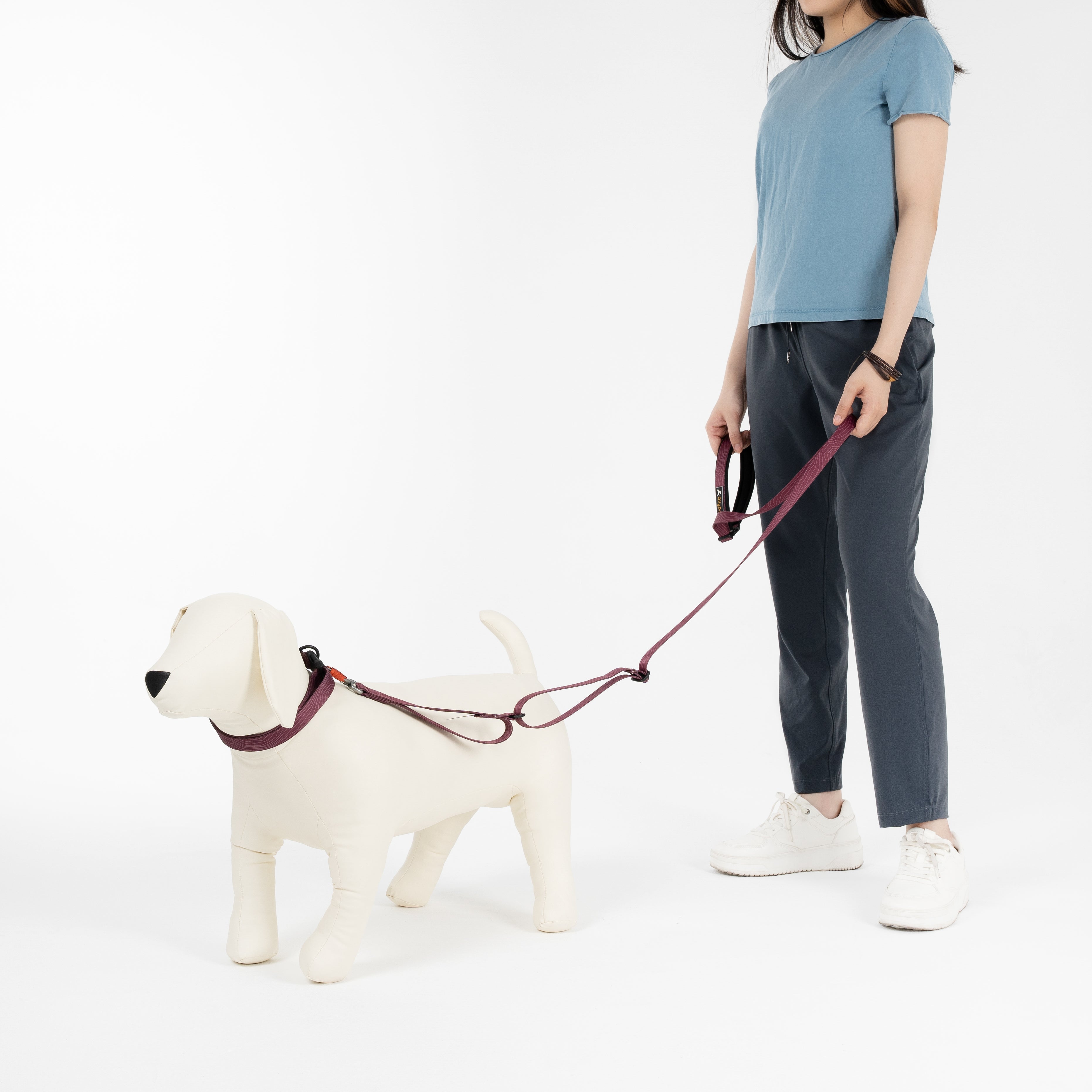 Person holding a leash attached to a mannequin dog wearing the OllyDog Flagstaff Dog Collar in Rosewood woodgrain, shown in a white studio setting with full-body view #color_rosewood woodgrain