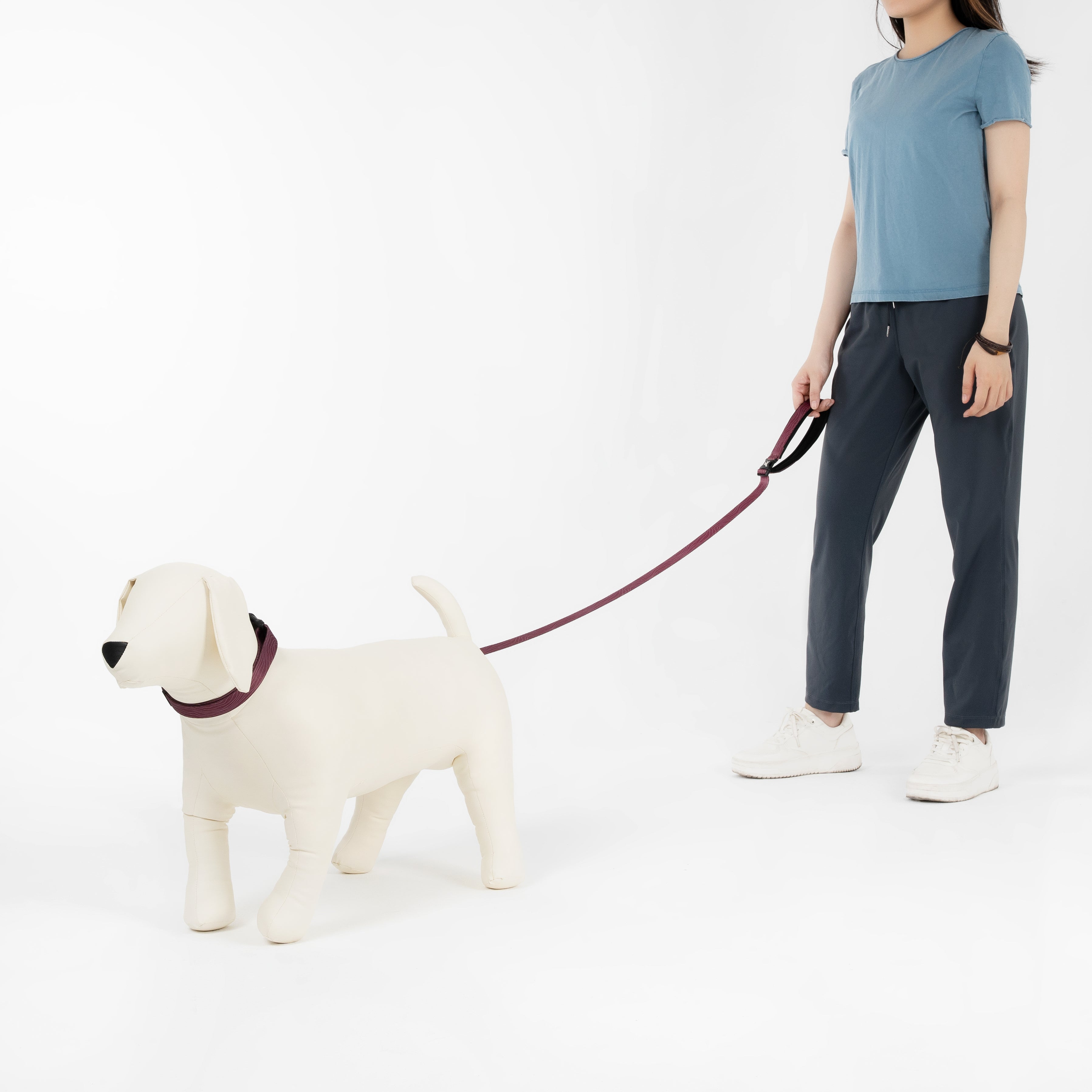 Person holding a leash attached to a mannequin dog wearing the OllyDog Flagstaff Dog Collar in Rosewood woodgrain, full-body side view in a white studio background #color_rosewood woodgrain