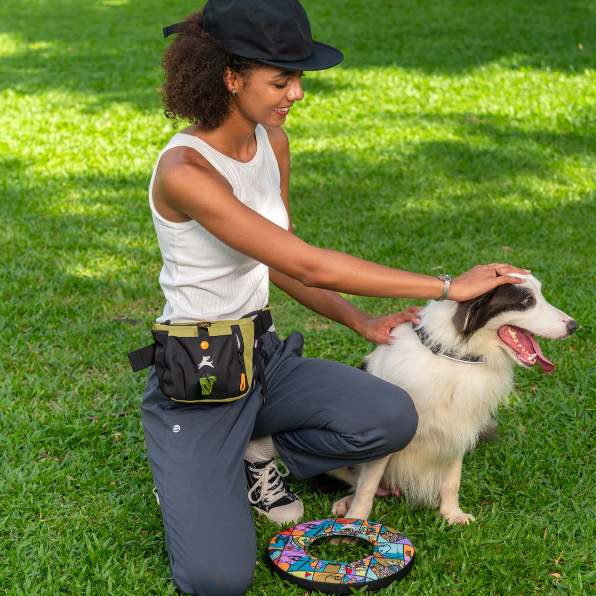 Lifestyle shot of a person wearing the OllyDog Backcountry Day Bag in alchemy color around their waist while kneeling and petting a dog on the grass outdoors. #color_alchemy