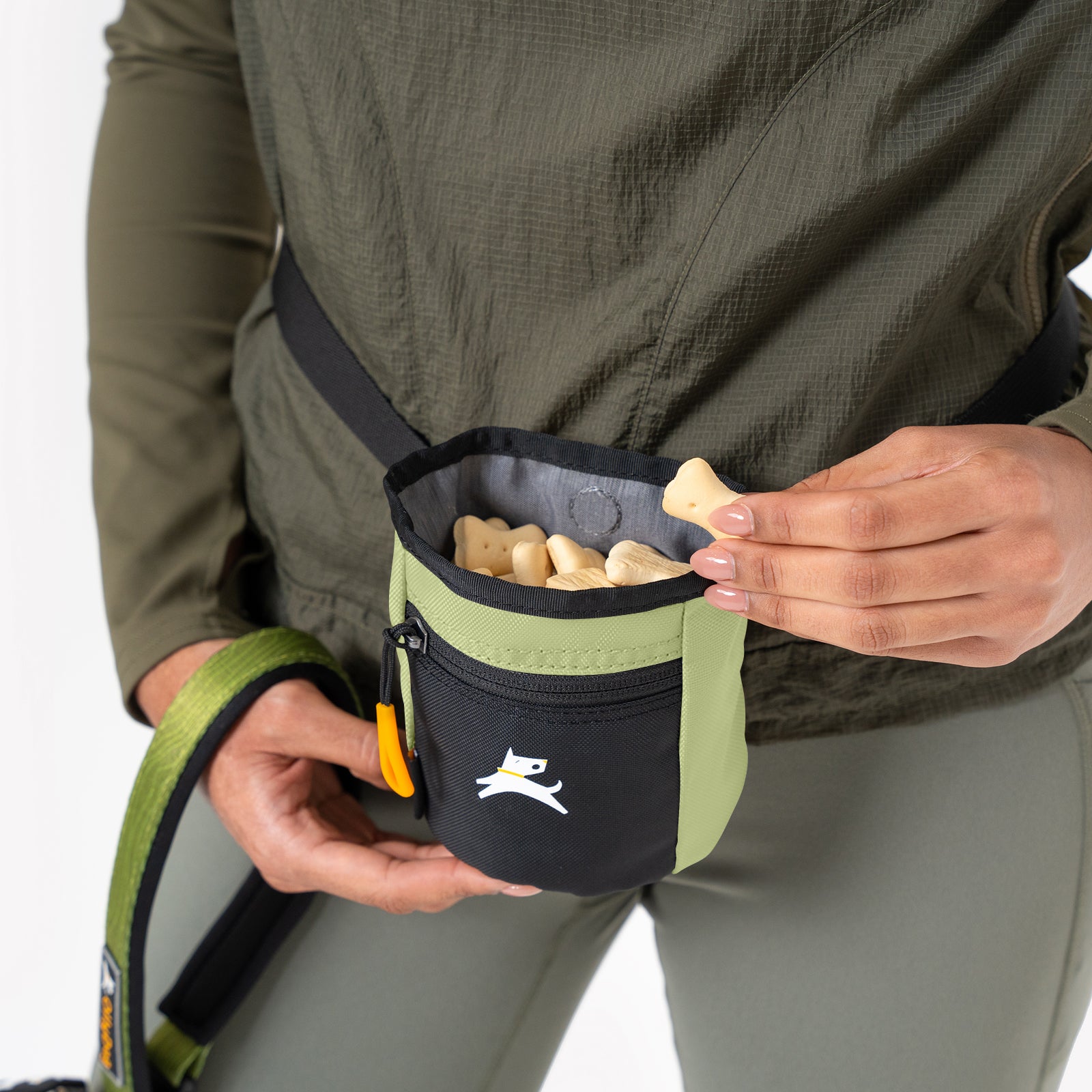 Close-up of a person wearing the OllyDog Goodie Treat Bag in palm color around their waist and reaching inside for a dog training treat. #color_palm